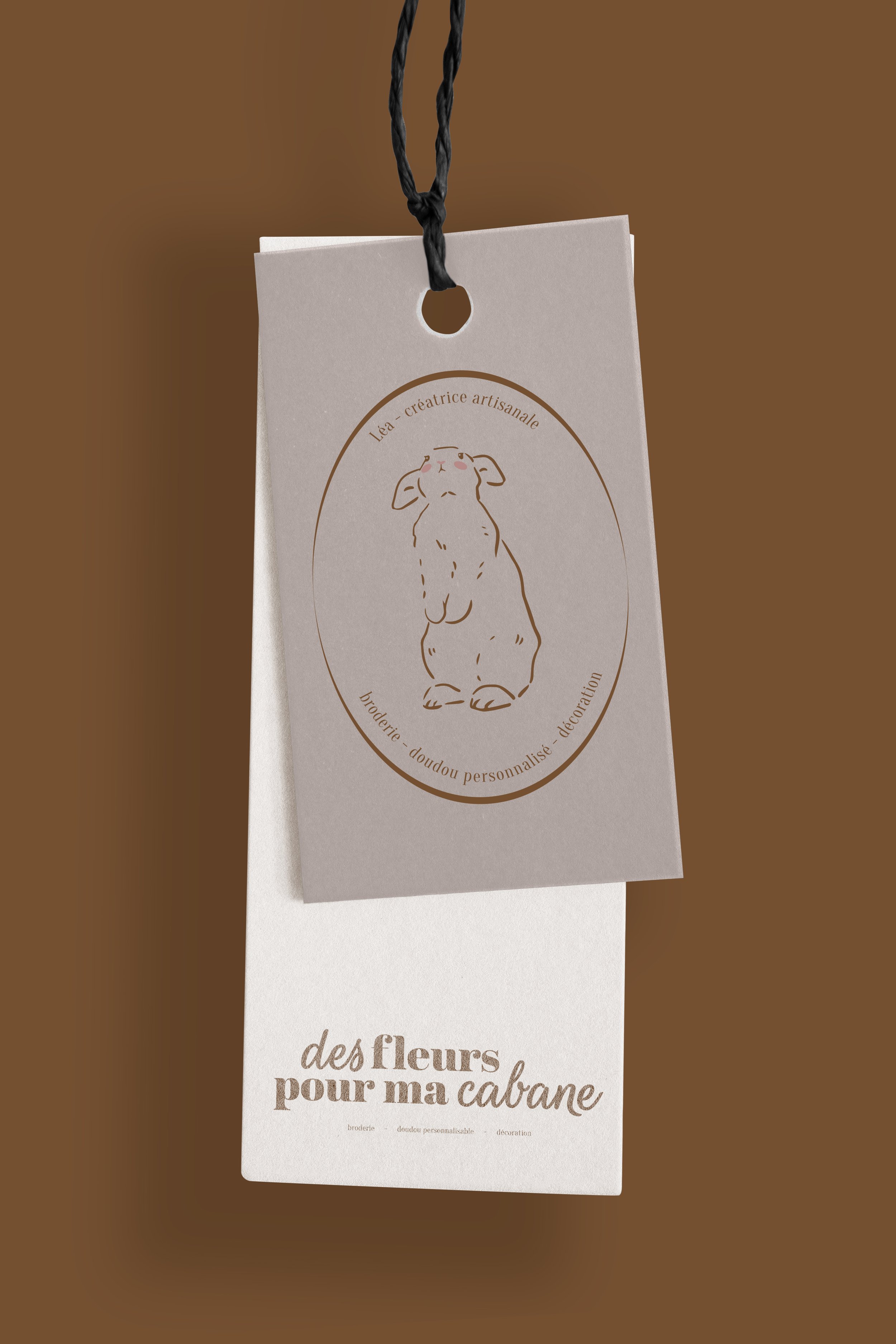 Deux étiquettes suspendues, l'une avec un dessin d'un lapin et l'autre avec le texte "des fleurs pour ma cabane". Les étiquettes semblent être pour une boutique artisanale ou une création personnalisée.