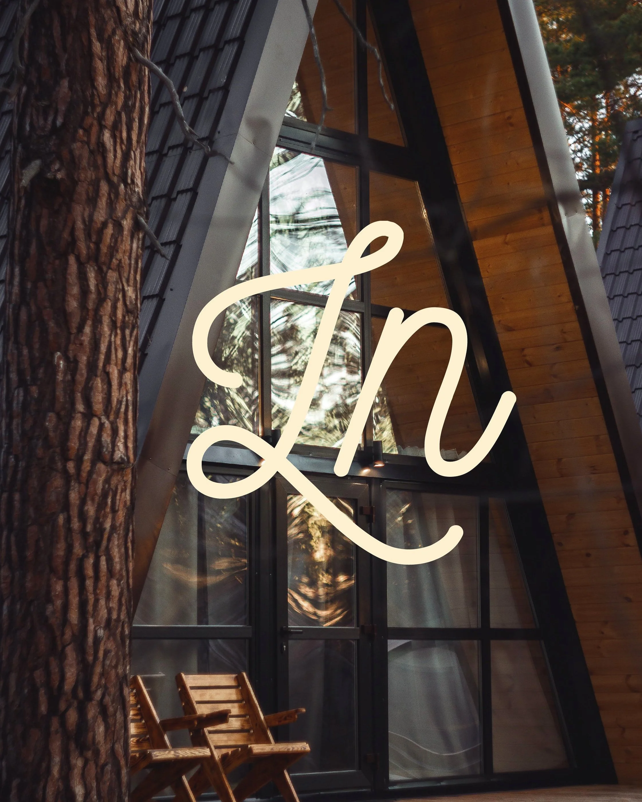 Une cabane en bois avec un toit en pente, de grandes fenêtres en verre, entourée d'arbres, avec deux chaises en bois au premier plan.