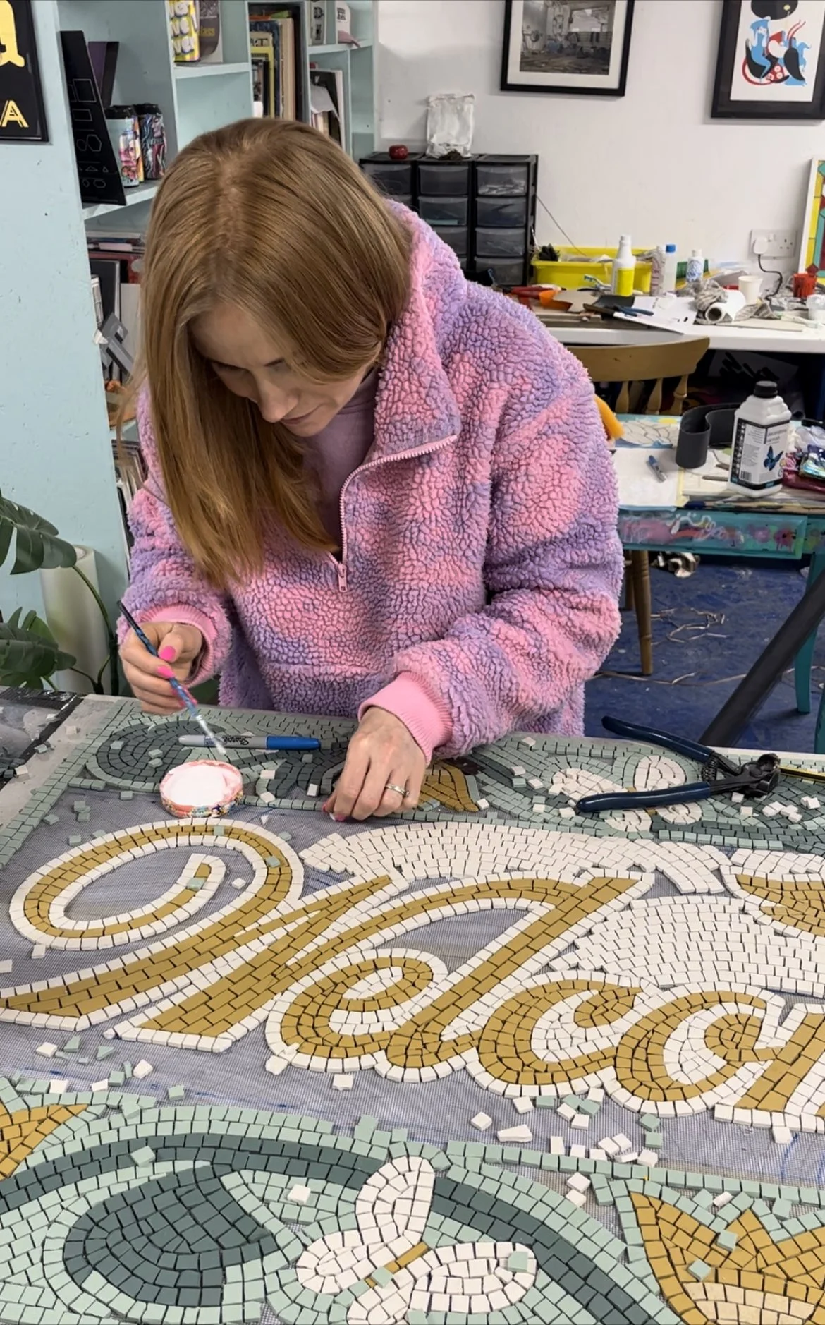 Person working on a mosaic art project with the word 'Welcome' in a creative studio.