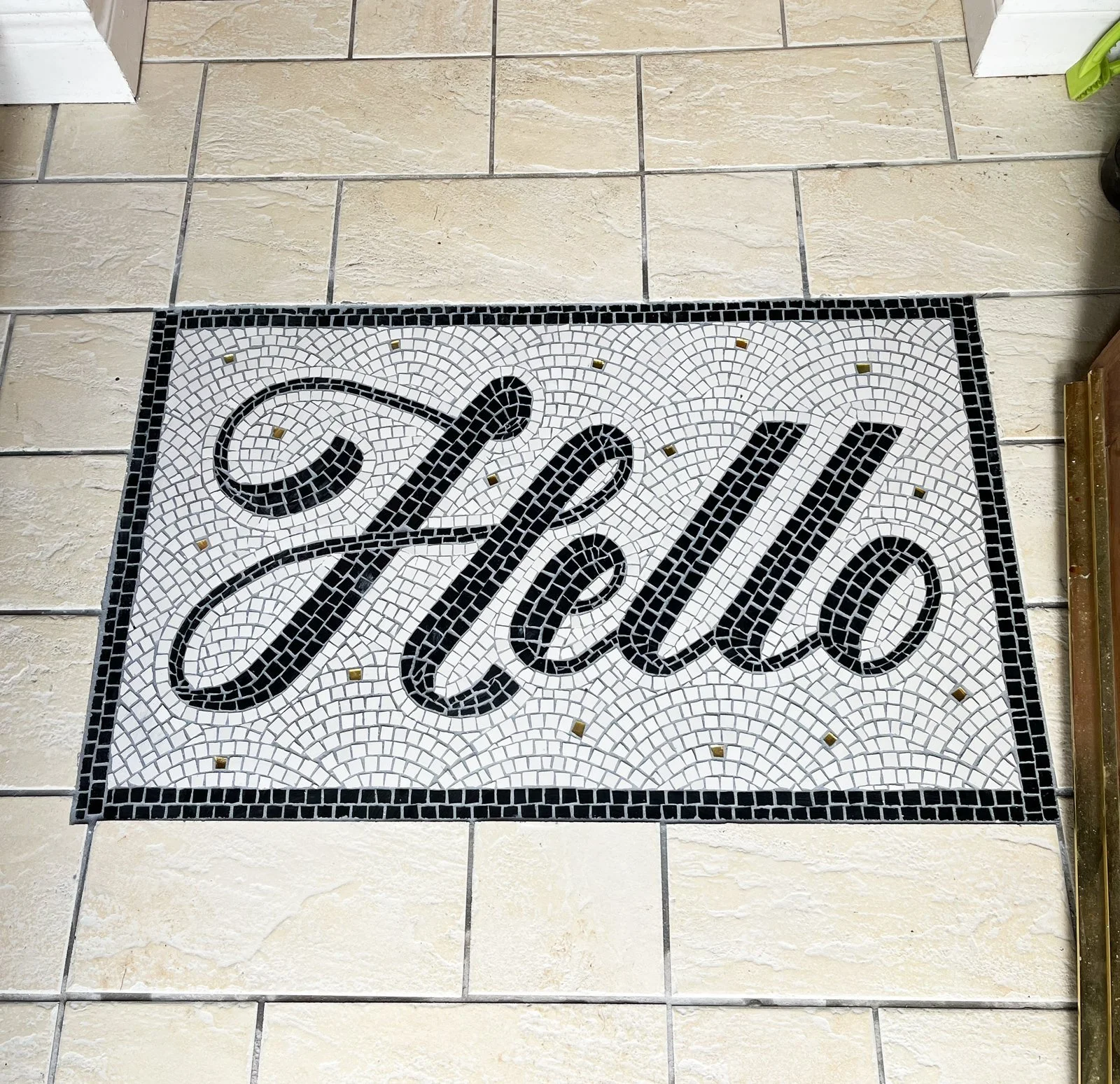 Entranceway mosaic with the word 'Hello' written in black cursive on a white background, bordered with small black tiles.