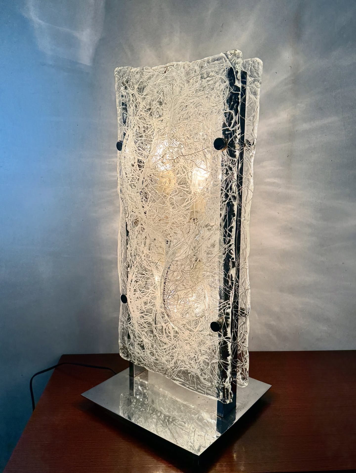 DISPONIBILE 🟢

Lampada scultorea a due facce in vetro di Toni Zuccheri per Mazzega, anni &rsquo;70.
Un oggetto che va oltre la funzione e si colloca nel territorio della scultura luminosa. Presenta una struttura architettonica in metallo cromato che