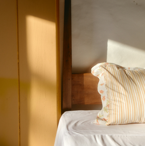 Morning sunlight across a pillow and white sheets on a wooden bed