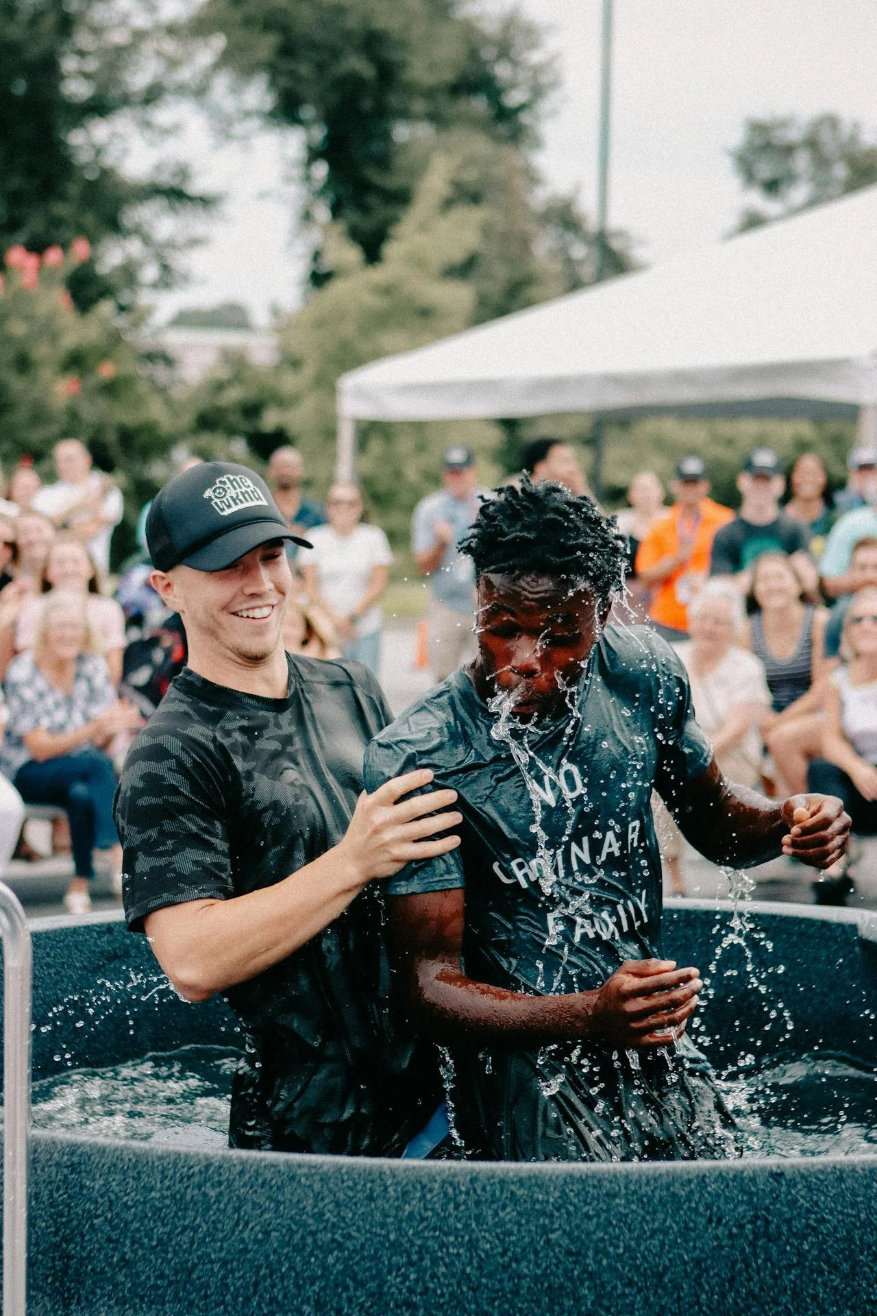 A person splashes water on another person during an outdoor event with a crowd of onlookers in the background.