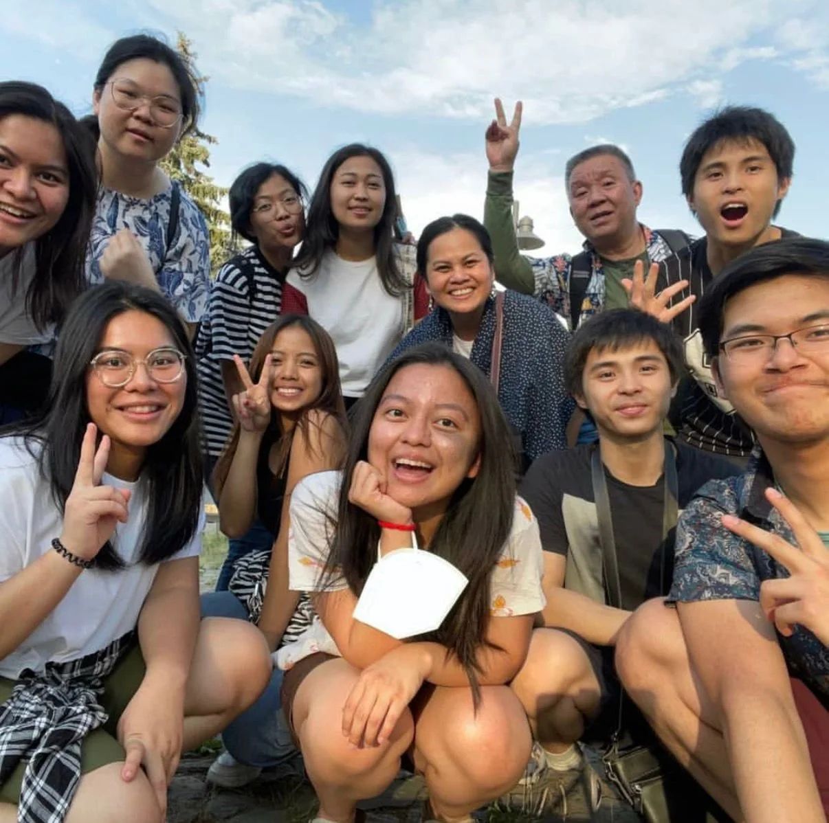 Group of people smiling and posing outdoors with blue sky in background.