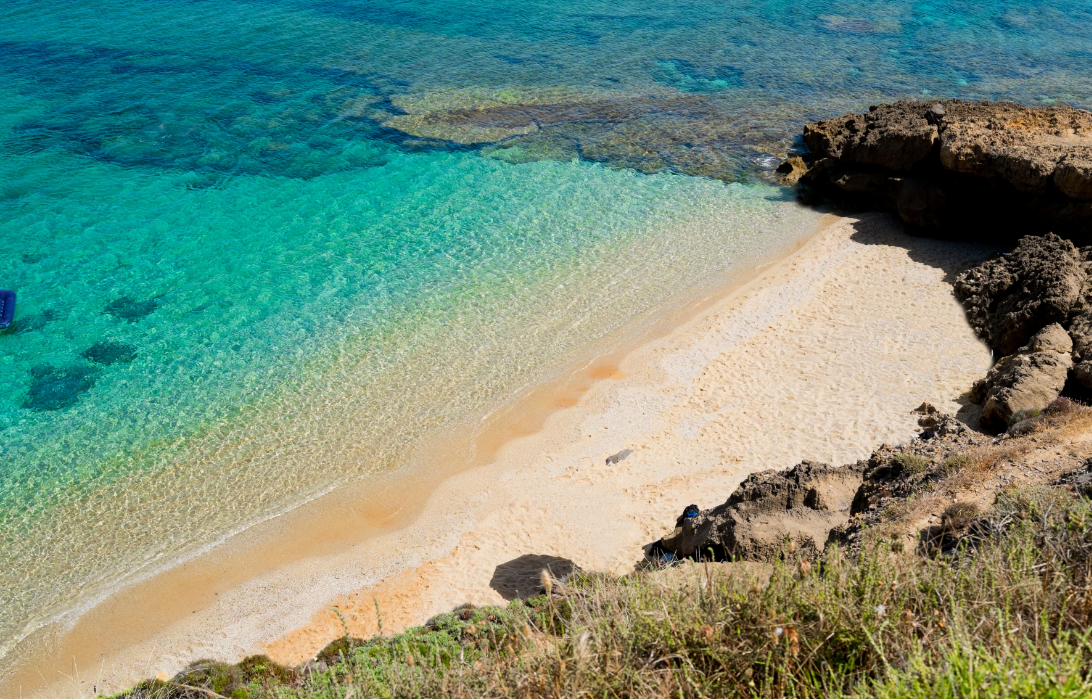 A sandy beach with clear turquoise water and rocks along the shoreline