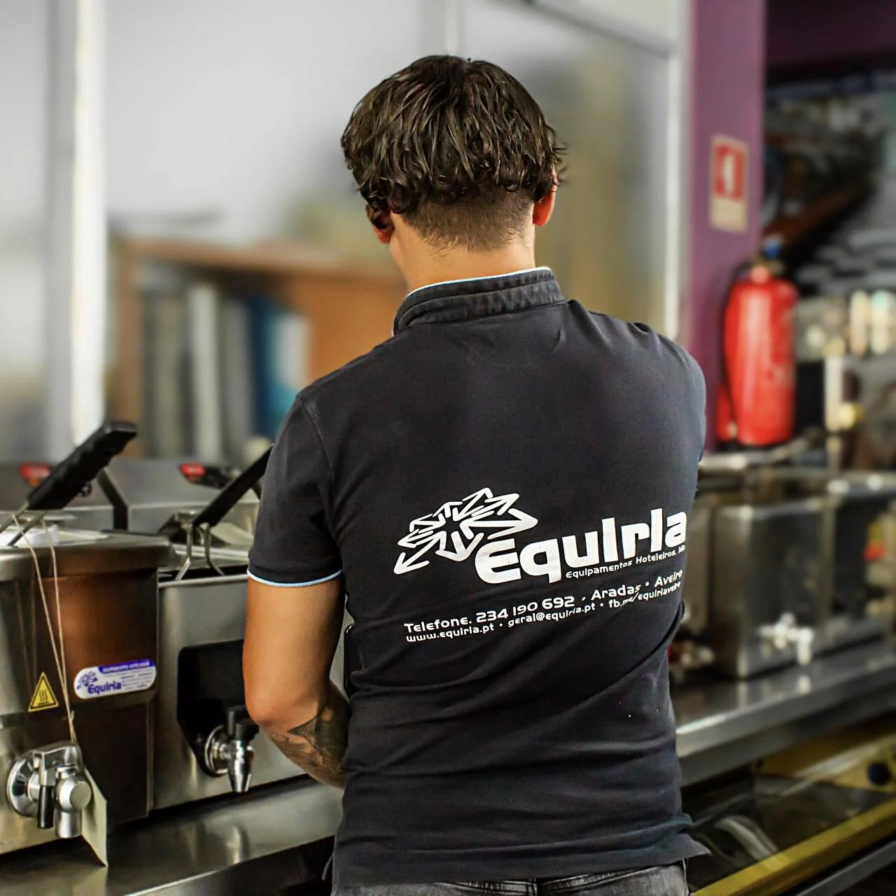 Mulher com chapéu e mochila amarela ao lado de um rio com barcos e prédios ao fundo.