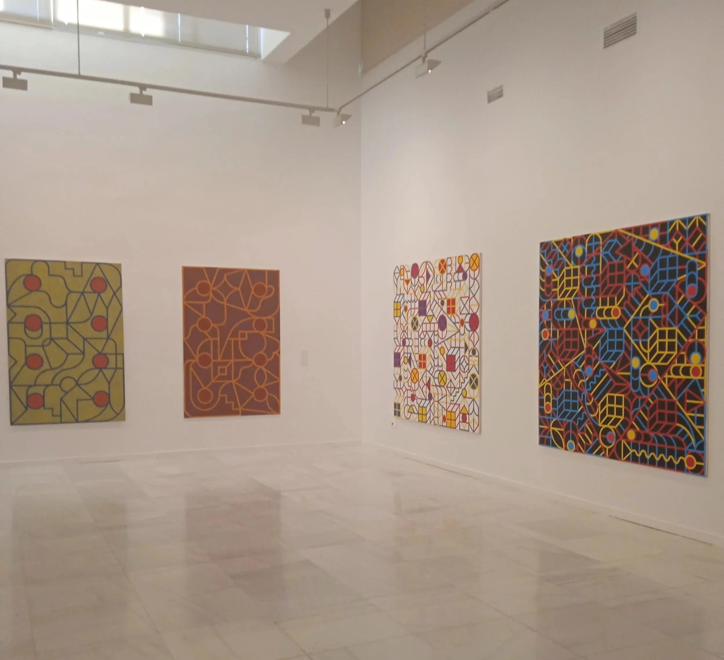 Cuatro cuadros con arte abstracto en una galería de paredes blancas y piso de mármol.