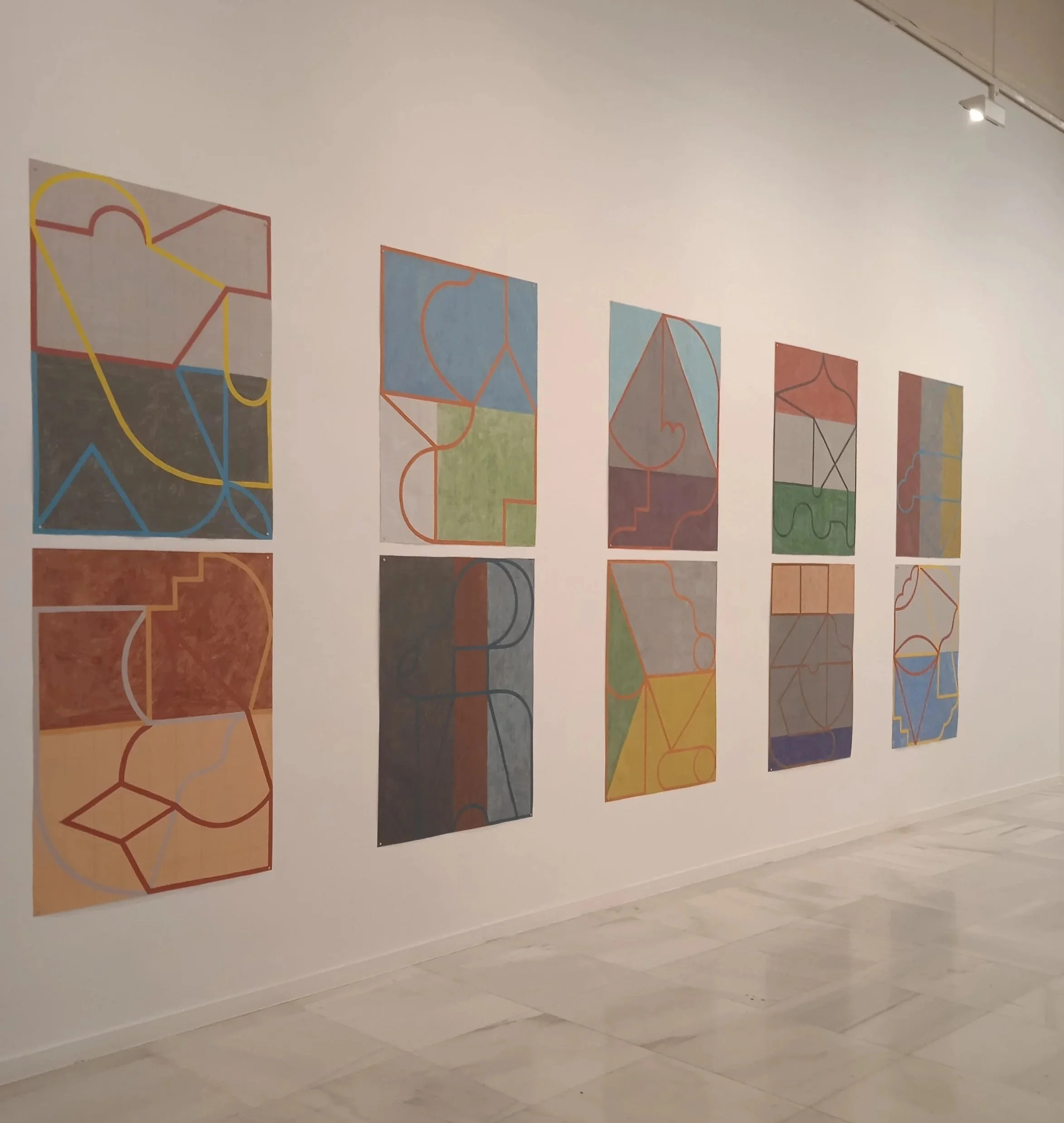 Serie de diez cuadros abstractos con líneas curvas y rectas de diferentes colores y fondos variados colgados en una pared blanca en una galería de arte.