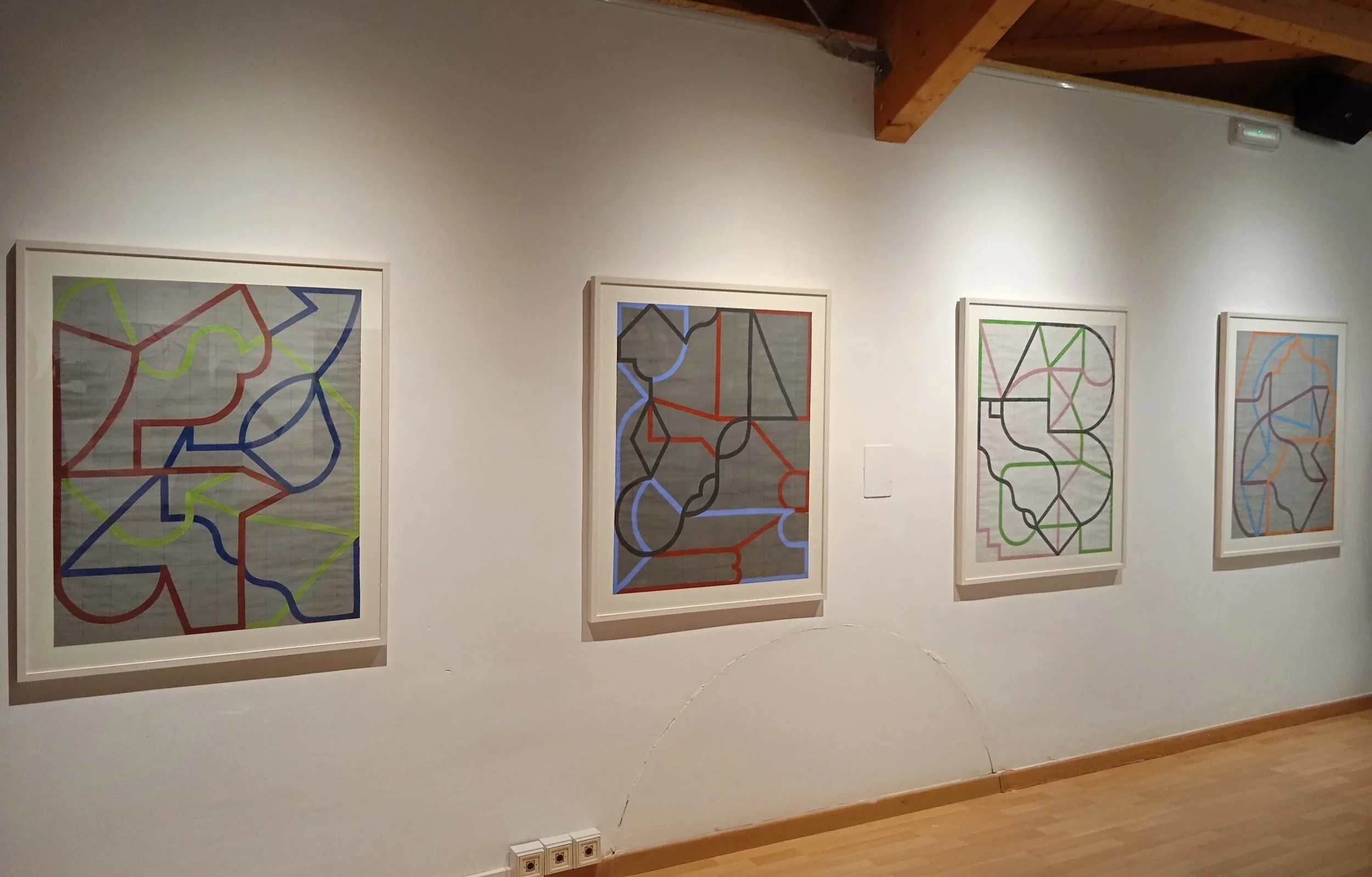 Cuatro cuadros abstractos con líneas de diferentes colores enmarcados en una pared en una galería de arte.