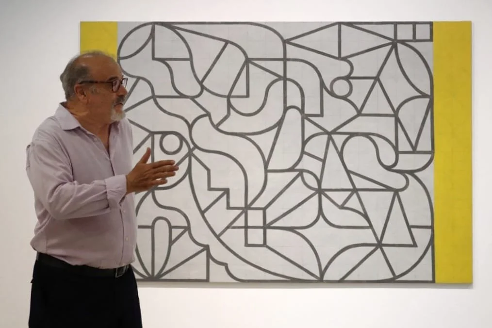 Hombre con gafas explica una obra de arte abstracta en un museo.