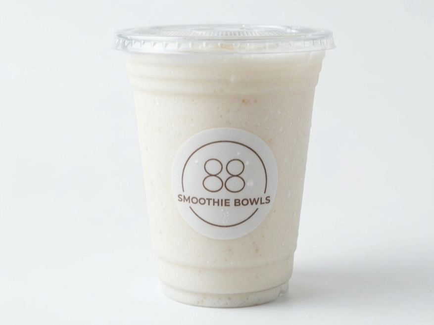 A clear plastic cup with a lid, filled with a creamy, pale-colored smoothie. The cup has a round logo with the number 88 and the words 'Smoothie Bowls' on it.