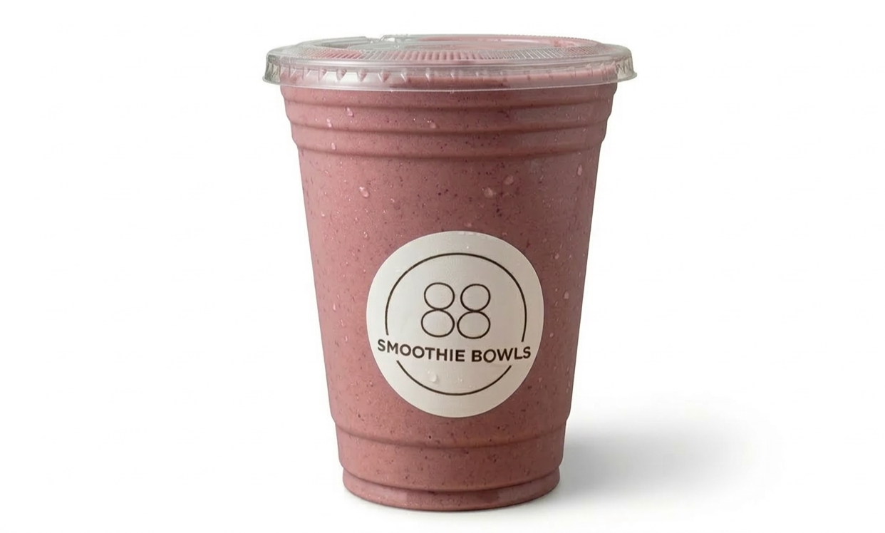 A pink smoothie in a clear plastic cup with a sealed lid, labeled 'Smoothie Bowls' and a logo of two circles inside a larger circle.