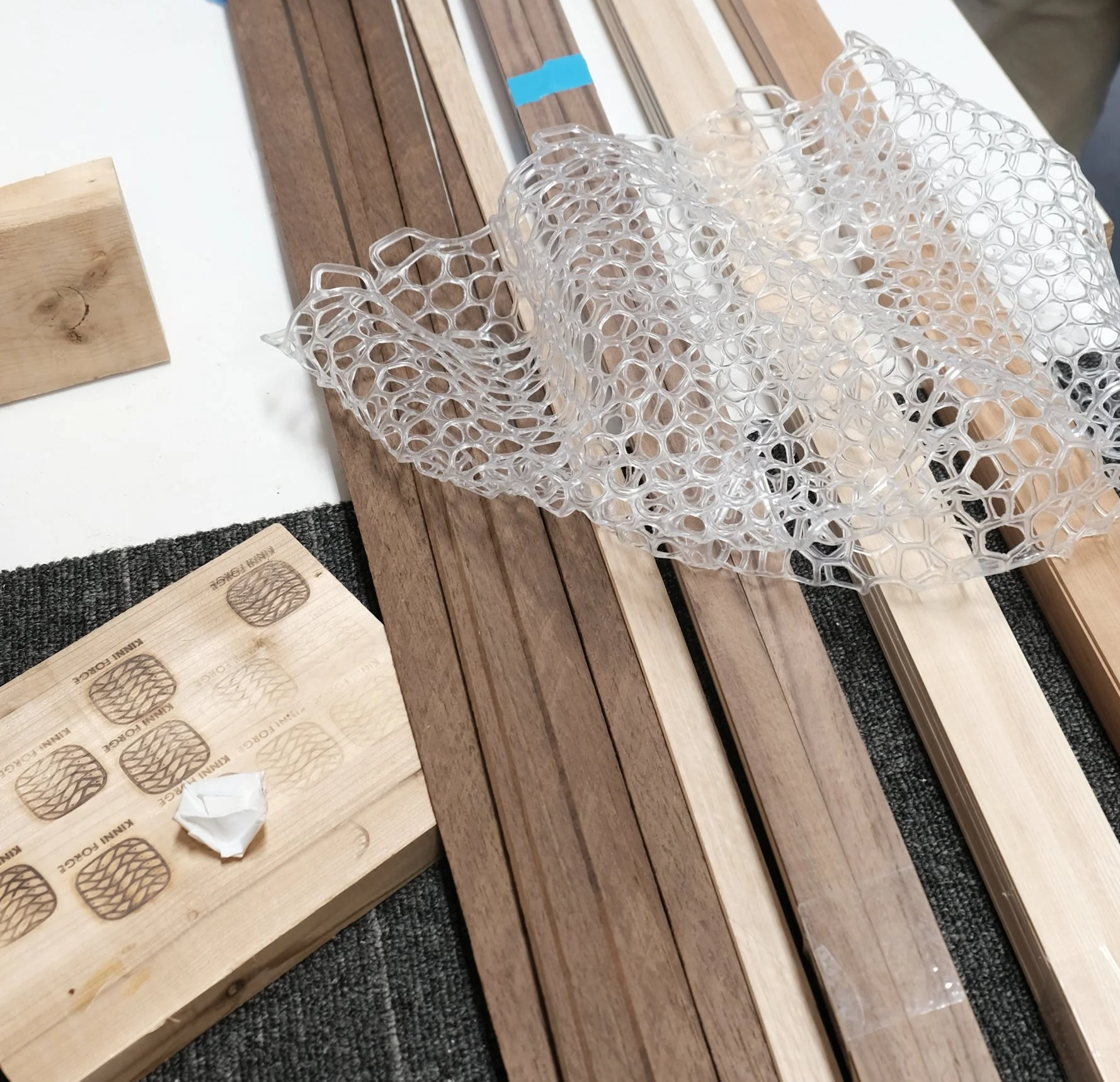 Various woodworking materials on a work surface, including wooden planks, a silicone net, and a sample piece of wood with stamped patterns.