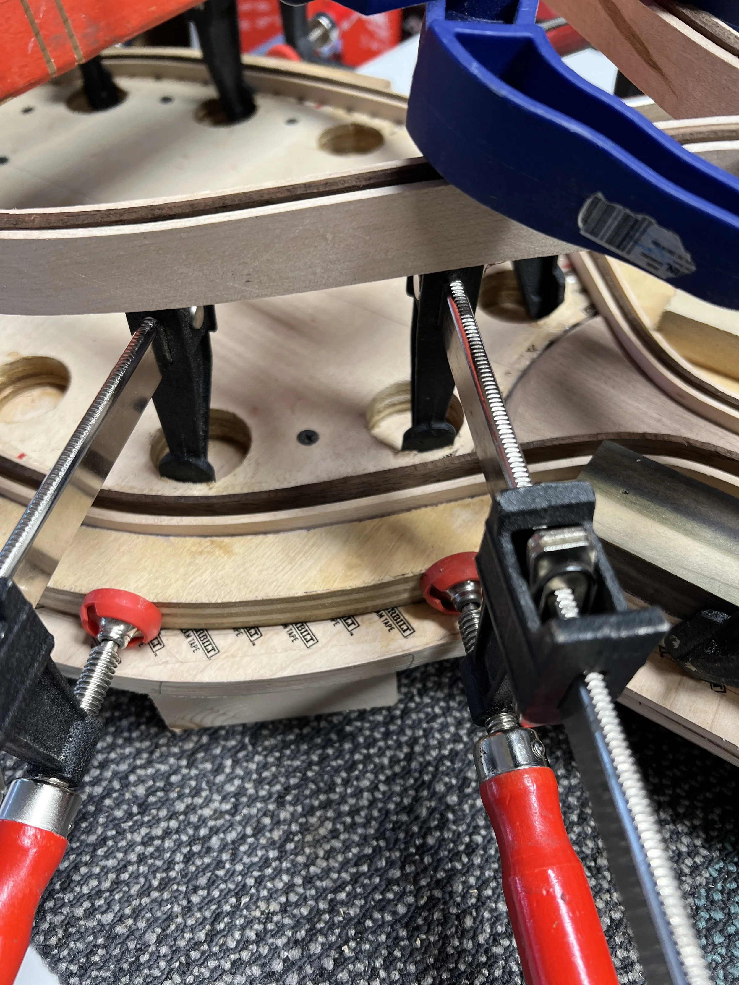 Clamps holding multiple layers of wood on a workbench.