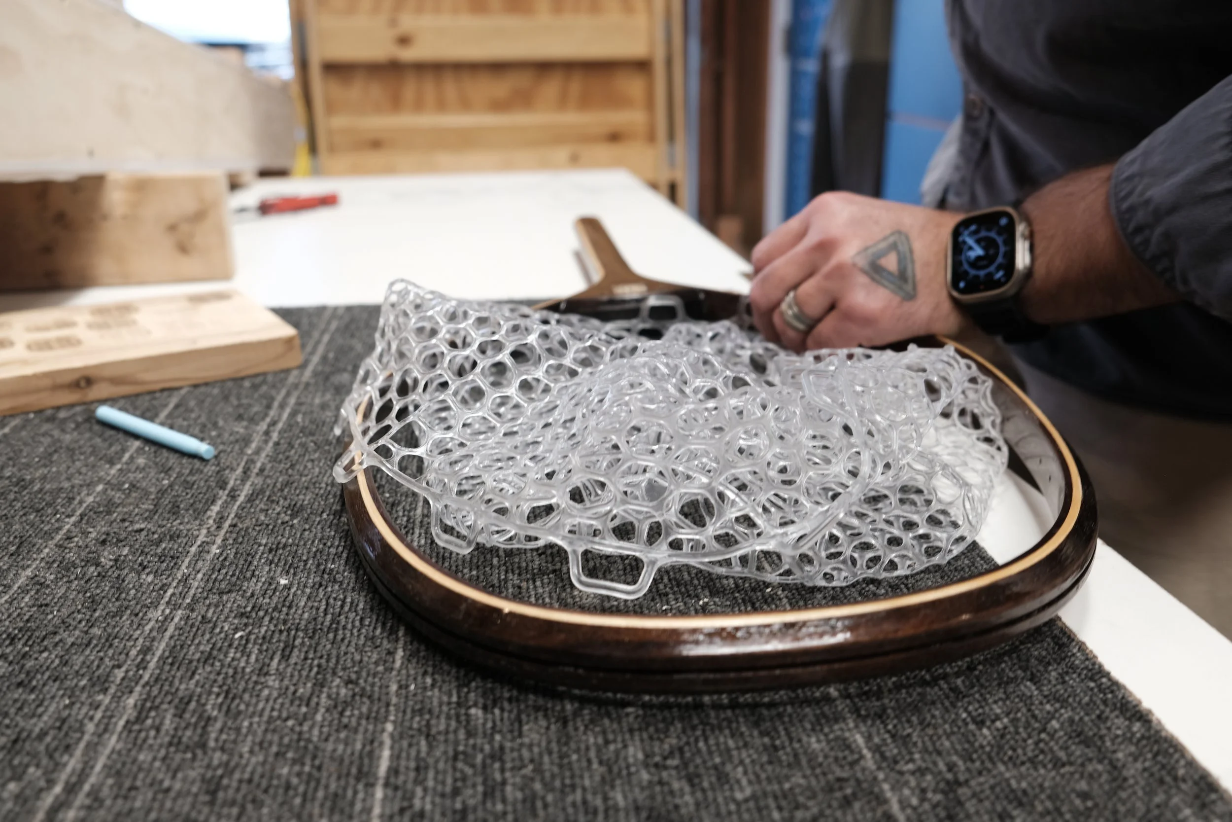 A person working with a complex, transparent 3D-printed object on a wooden tray in a workshop.