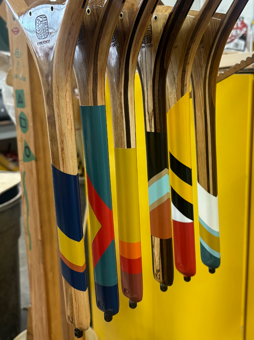 A display of colorful wood trout fishing net handles, each featuring a different multicolored painted design.