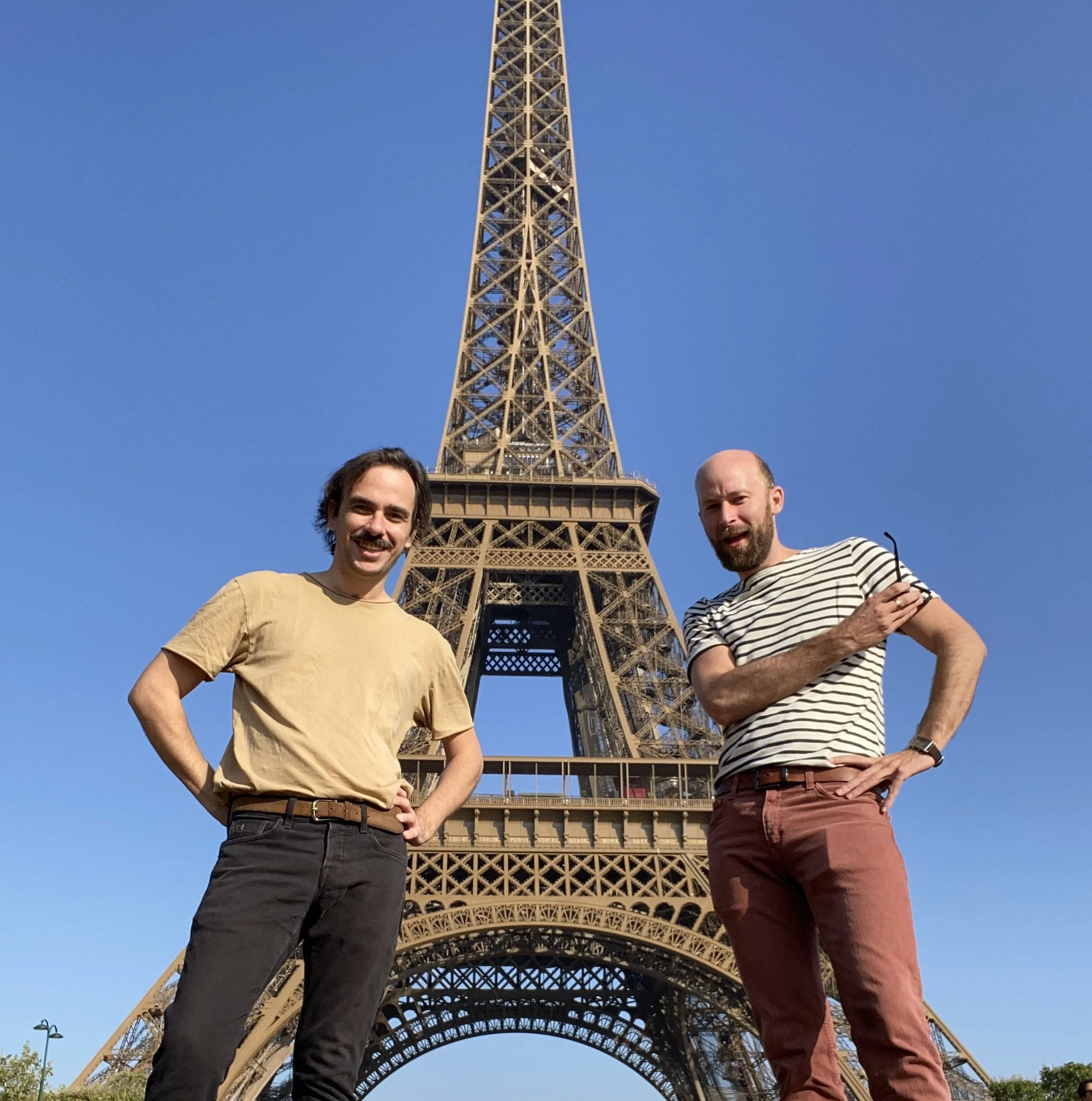 Two men standing in front of the Eiffel Tower during the daytime.