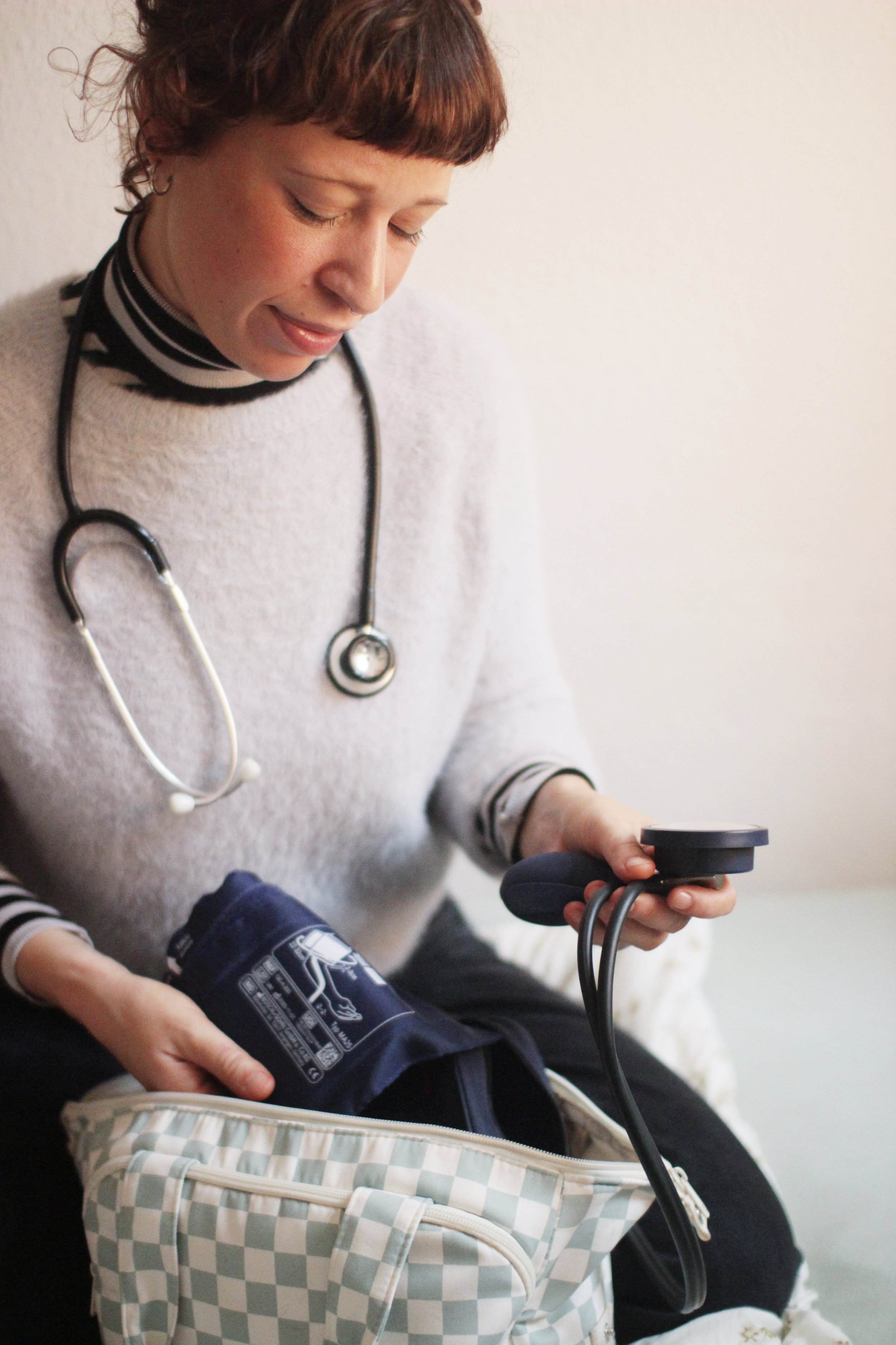 Hebamme Marie-Henrike Kruse hat ein Stethoskop um den Hals und ein Blutdruckmessgerät in der Hand. Sie misst den Blutdruck einer Person.