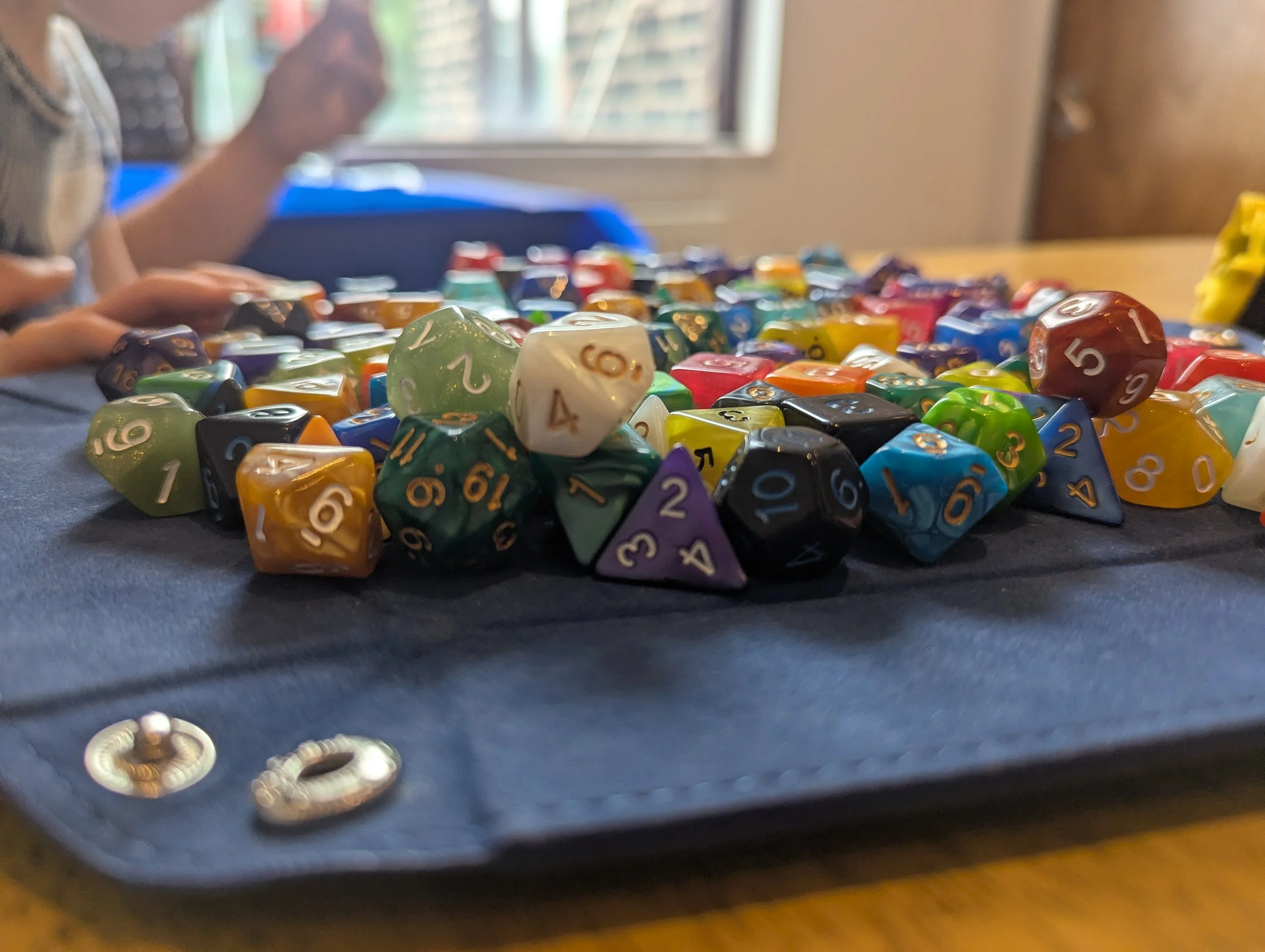 Close-up of a pile of multicolored polyhedral dice, some with numbers visible, on a dark surface with blurred background.