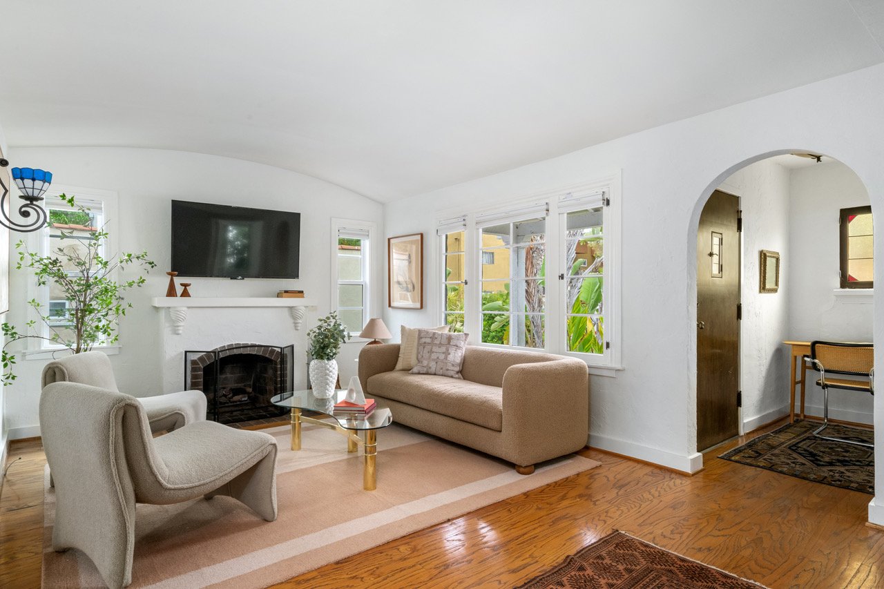 An interior view of a living room with hardwood floors, a fireplace, and soft window light all around.