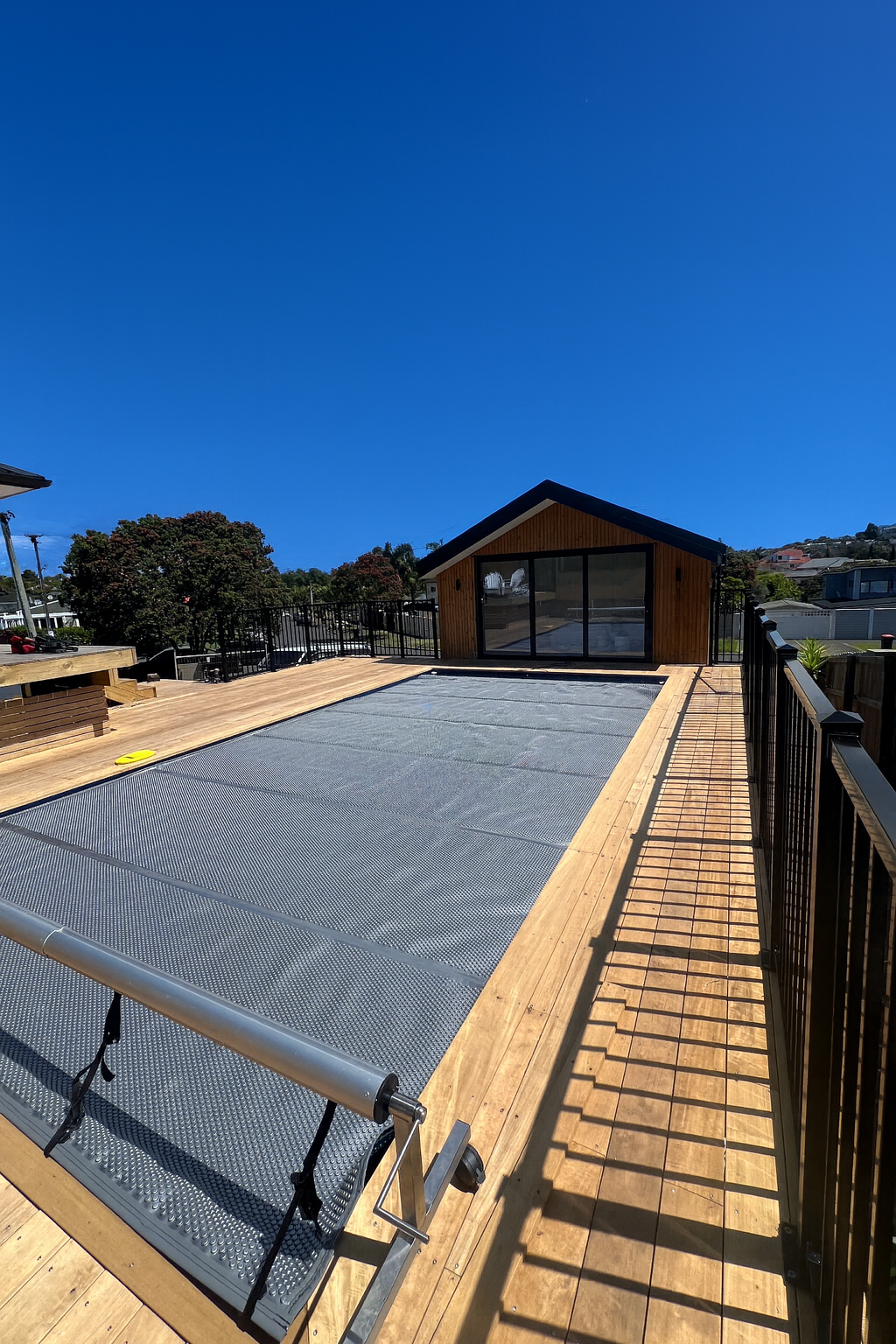 A rooftop deck with a screened-in area at the end, surrounded by black metal railing, under a clear blue sky.