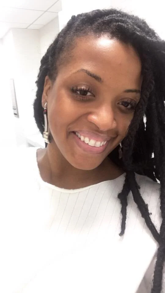 Close-up of Ashley Diaz, a smiling woman with dreadlocks, wearing earrings and a white top.