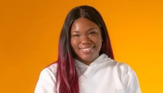 Kyla Shine, a young woman with long black and magenta hair, smiling against a yellow background.