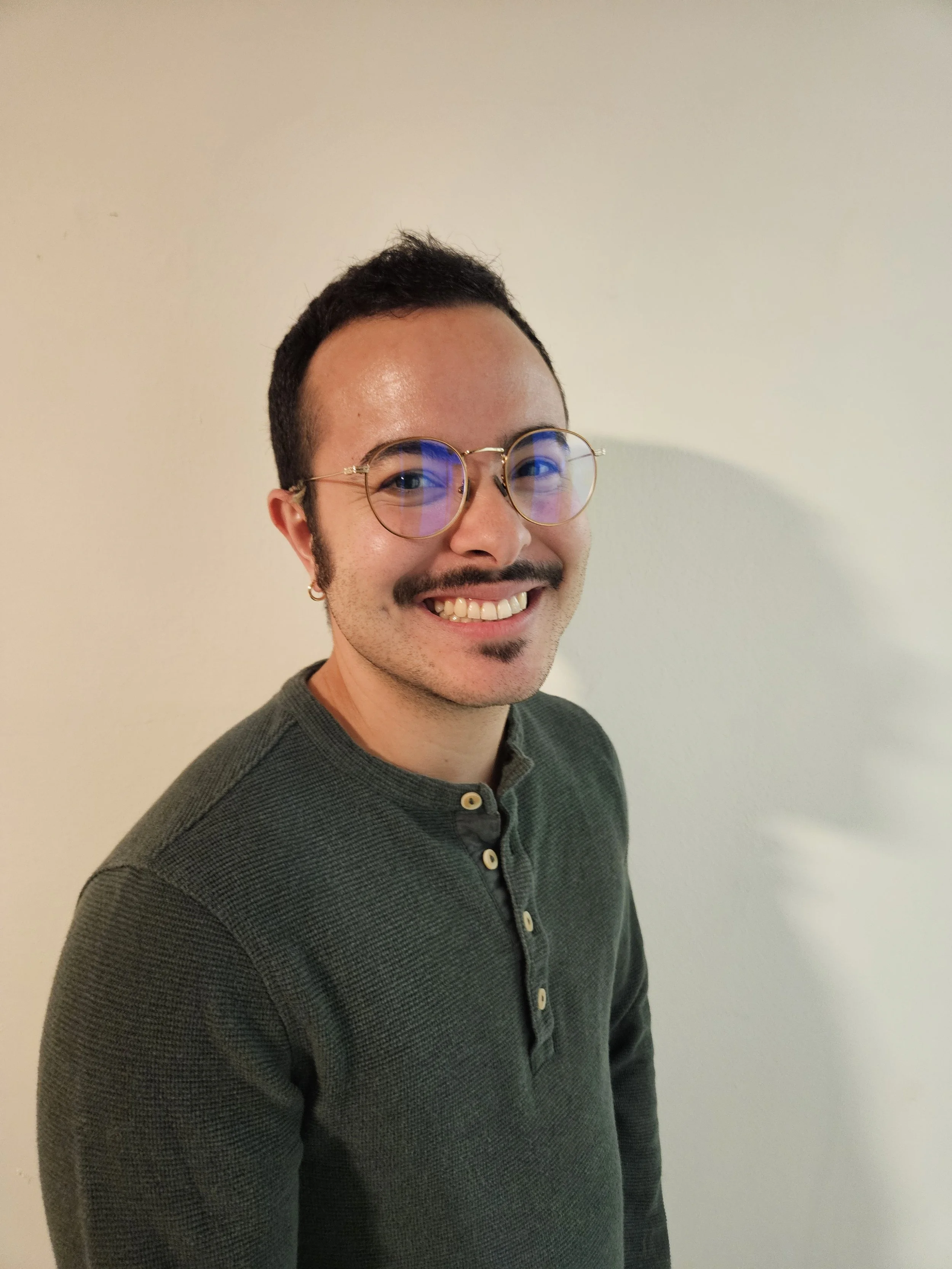 Milo Leon, a smiling man with glasses and a mustache, wearing gold-rimmed glasses and a dark green henley.
