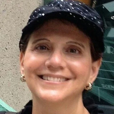 Close-up of a woman smiling, wearing a dark cap and earrings.