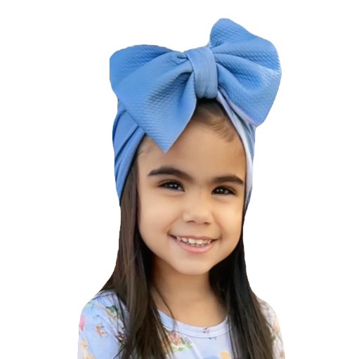 Child wearing a large blue hair bow and floral shirt, smiling.