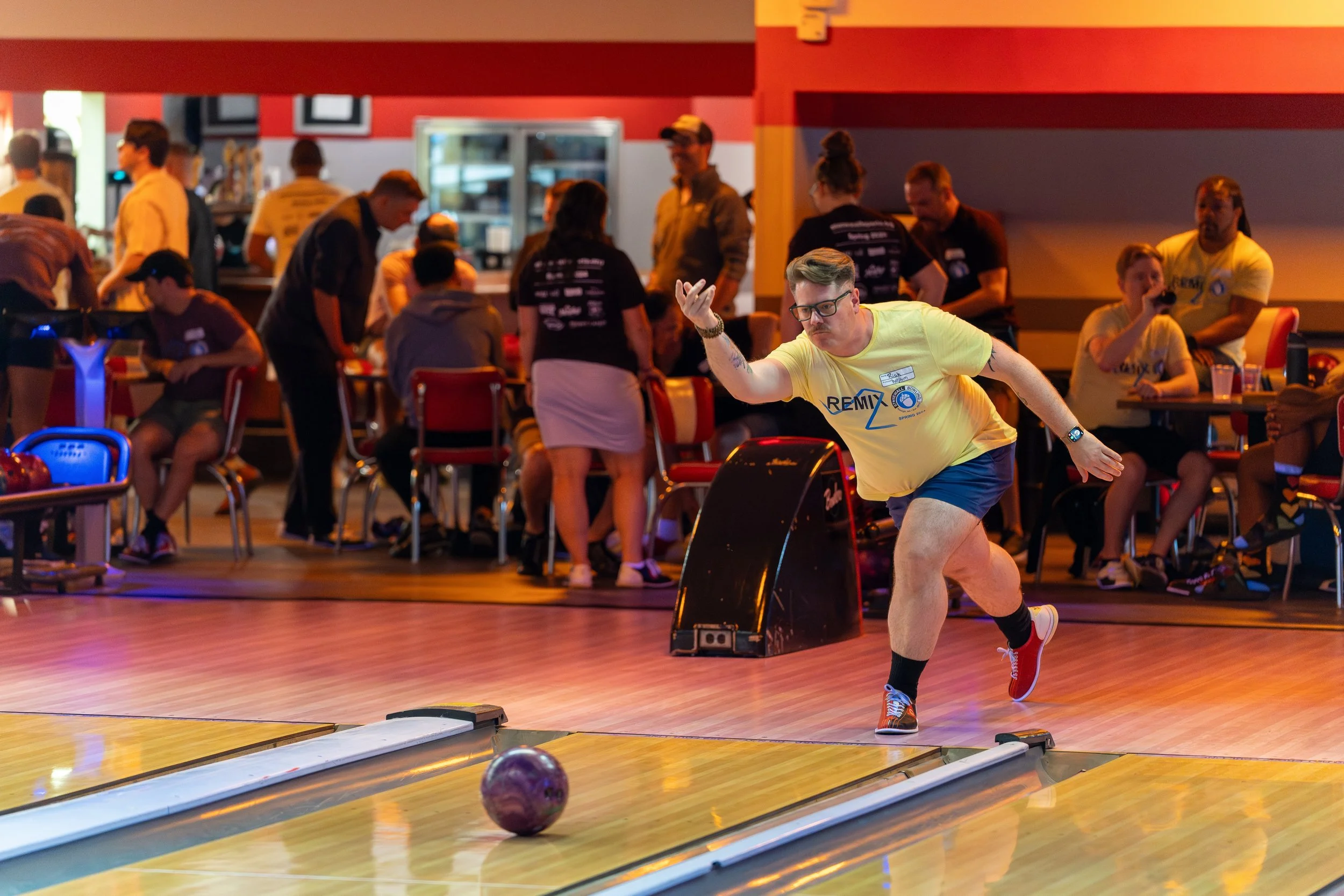 A person bowling in an alley, surrounded by people socializing.