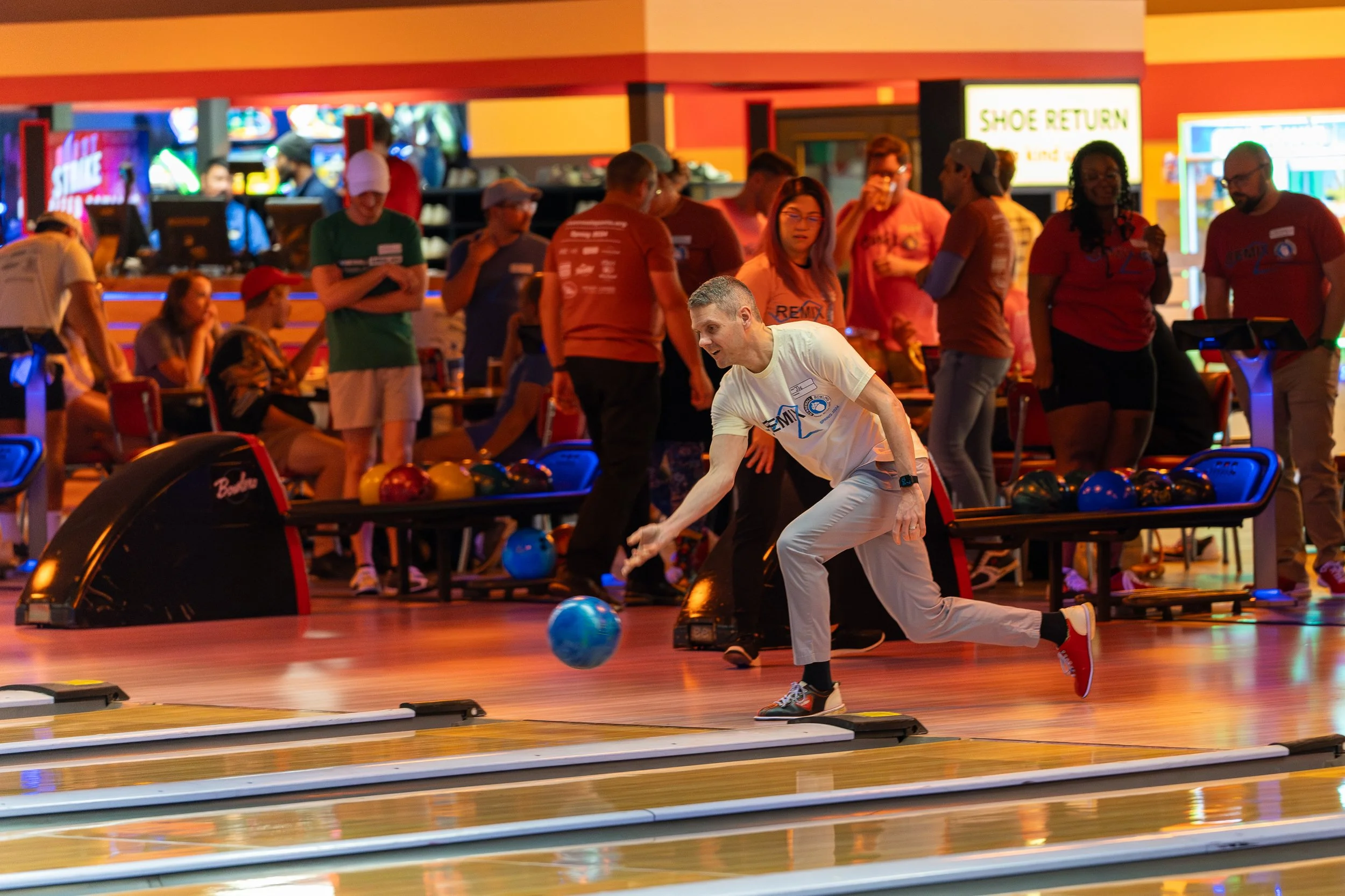 Group of people bowling in a bowling alley, focusing on a person releasing a bowling ball down the lane.