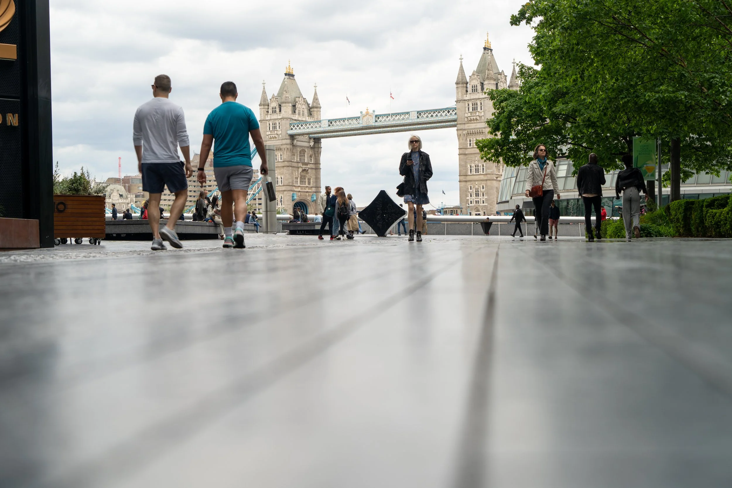 people walking near Tower Bridge, London, with cloudy sky and trees
