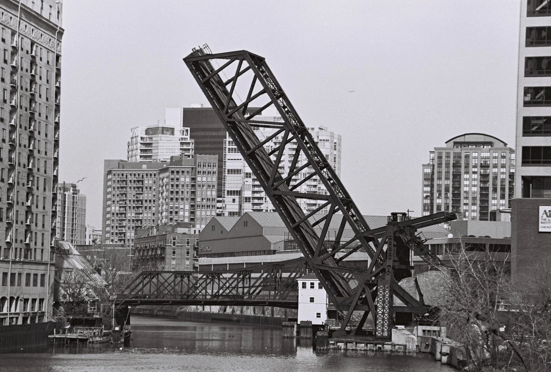 Black and white photo of a raised drawbridge in an urban setting with high-rise buildings in the background.