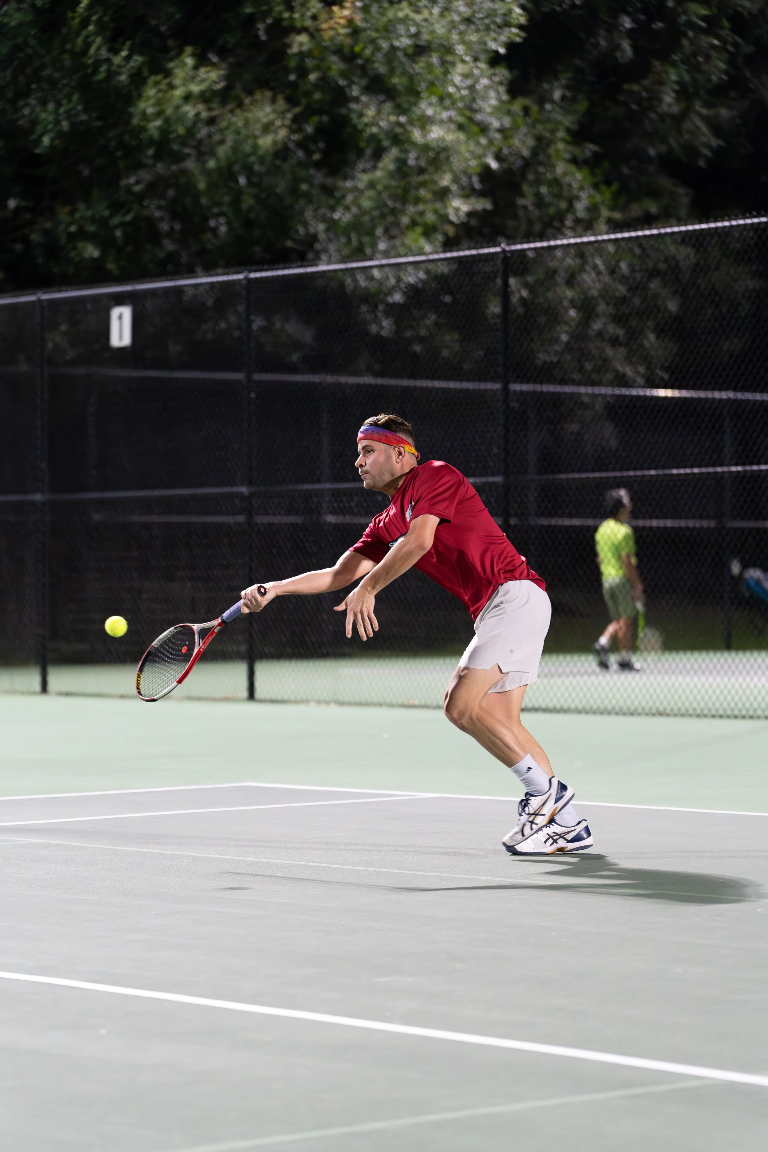 Tennis player in action hitting a forehand shot during a match on an outdoor court at night.