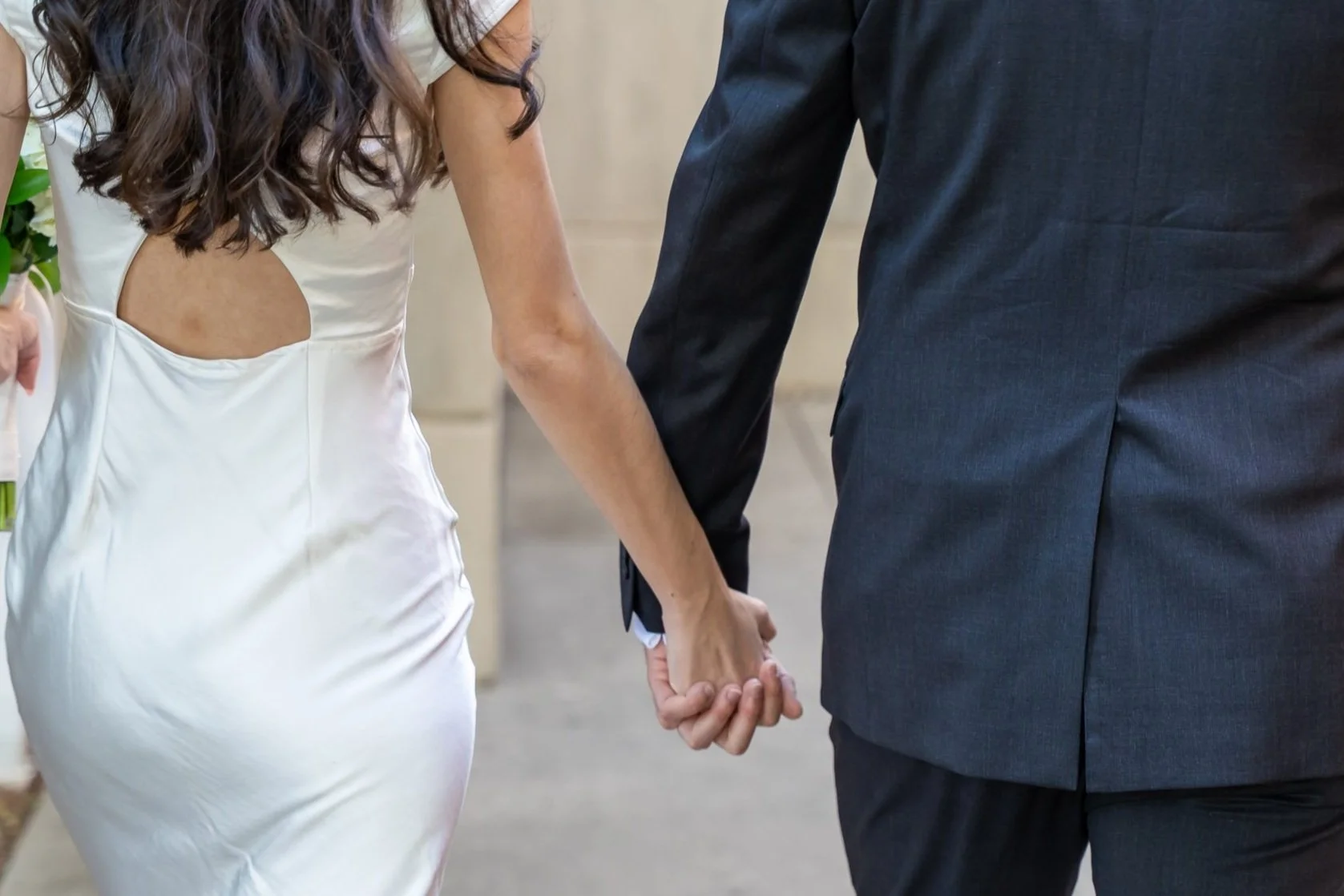 Couple holding hands, with a woman in a white dress and a man in a dark suit