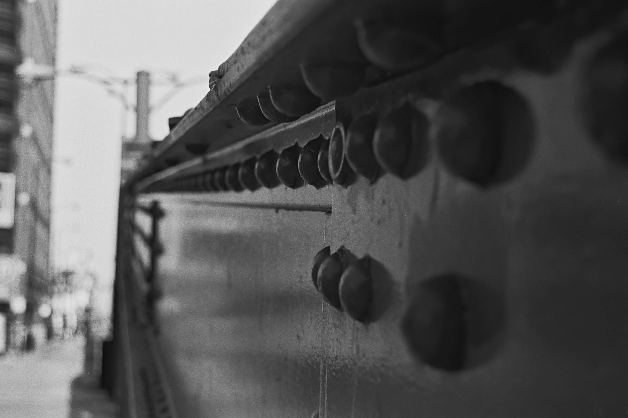Close-up of metal bridge rivets in black and white, with blurred urban background.