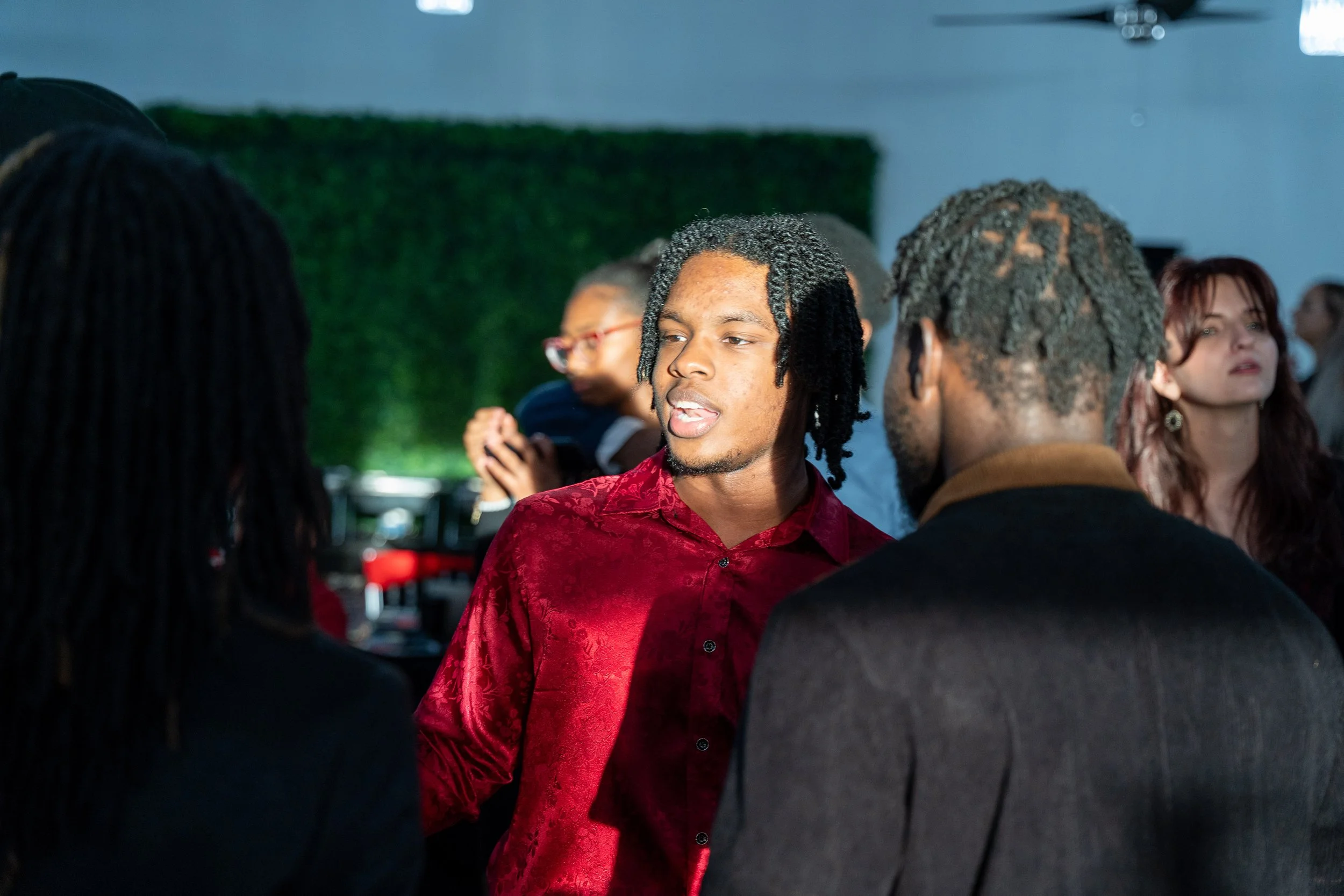 Group of people talking at a social gathering with greenery in the background.