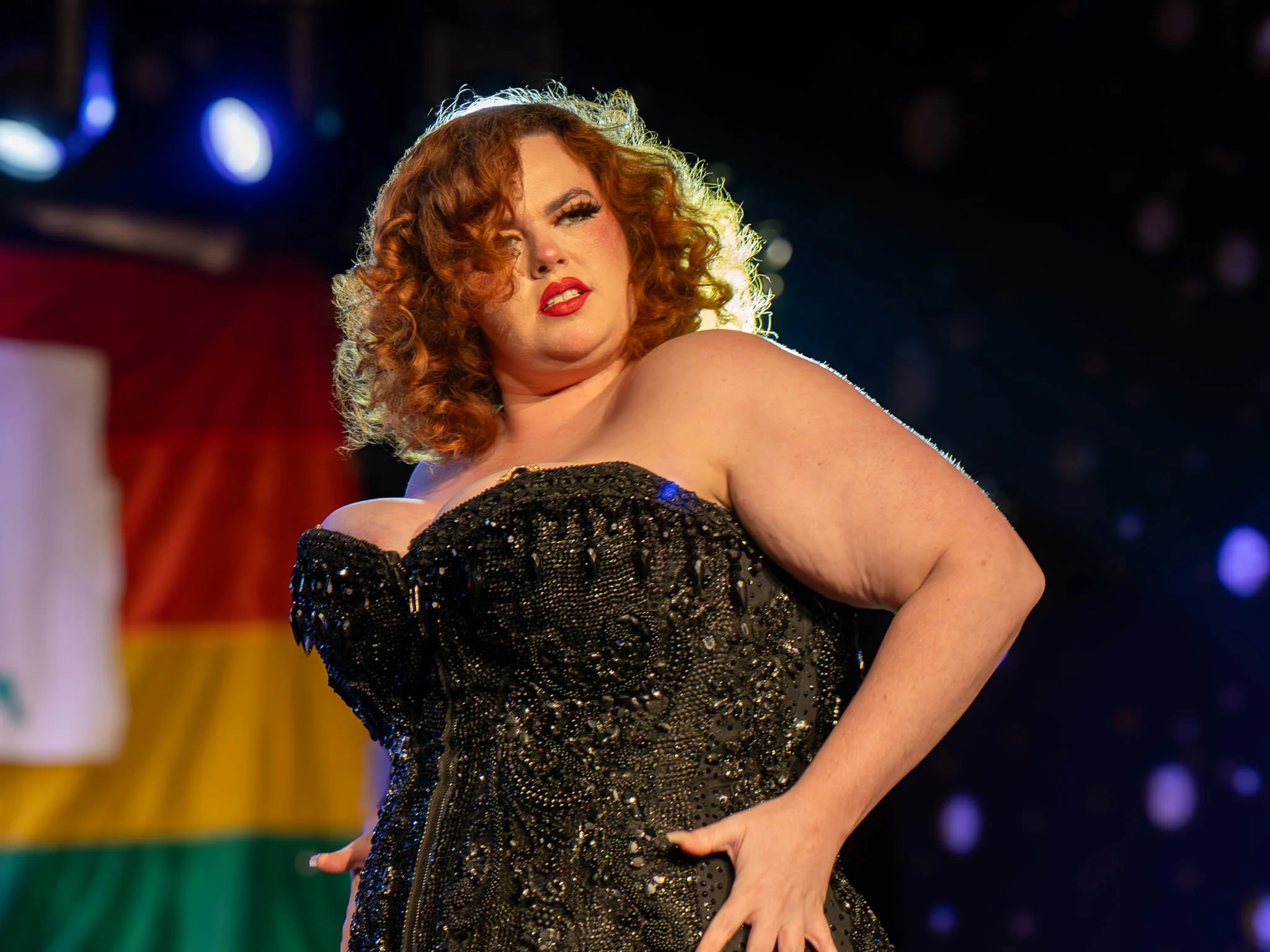Person with curly red hair wearing a black sequined dress on stage.