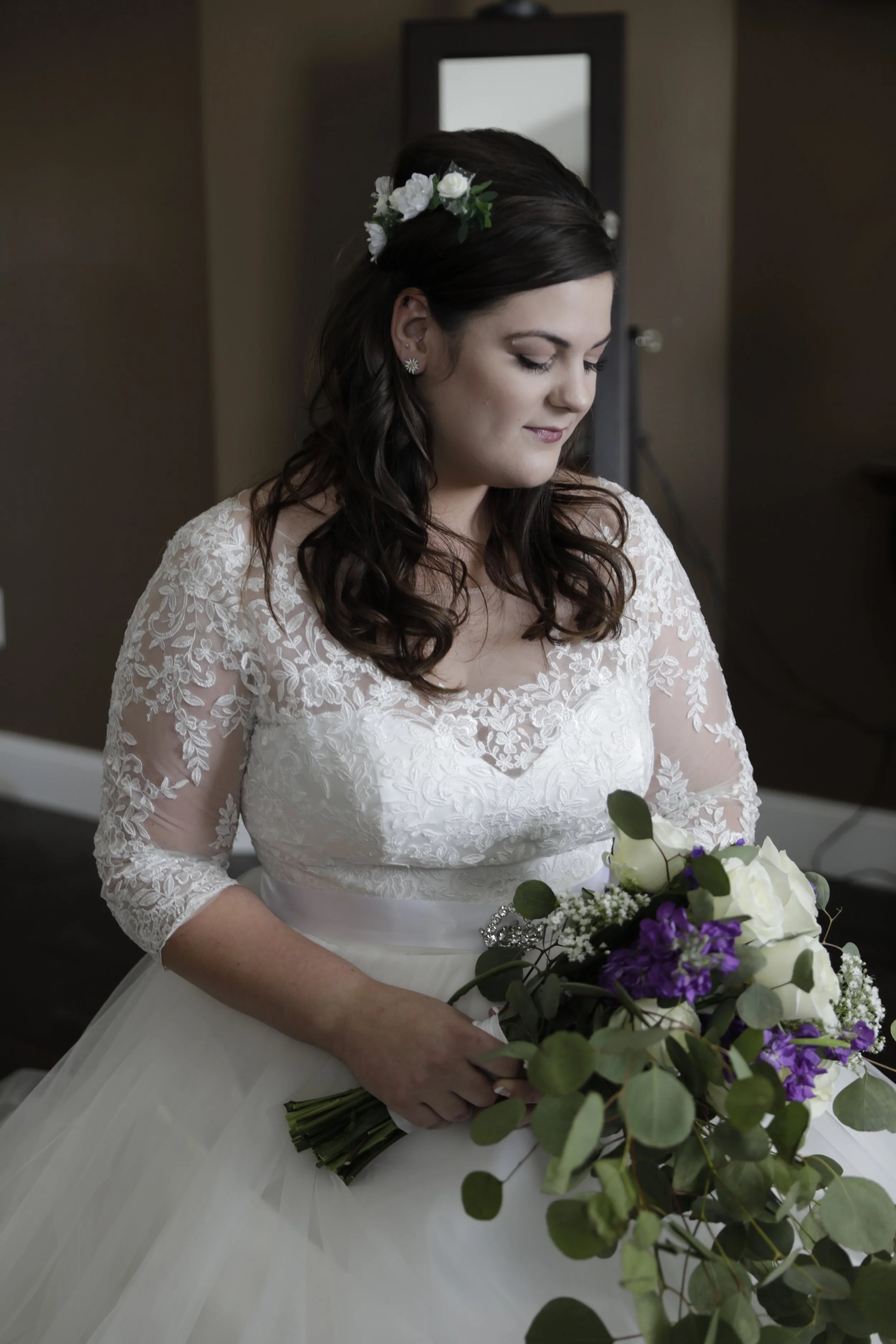 Bride in lace wedding dress holding a bouquet with purple and white flowers.