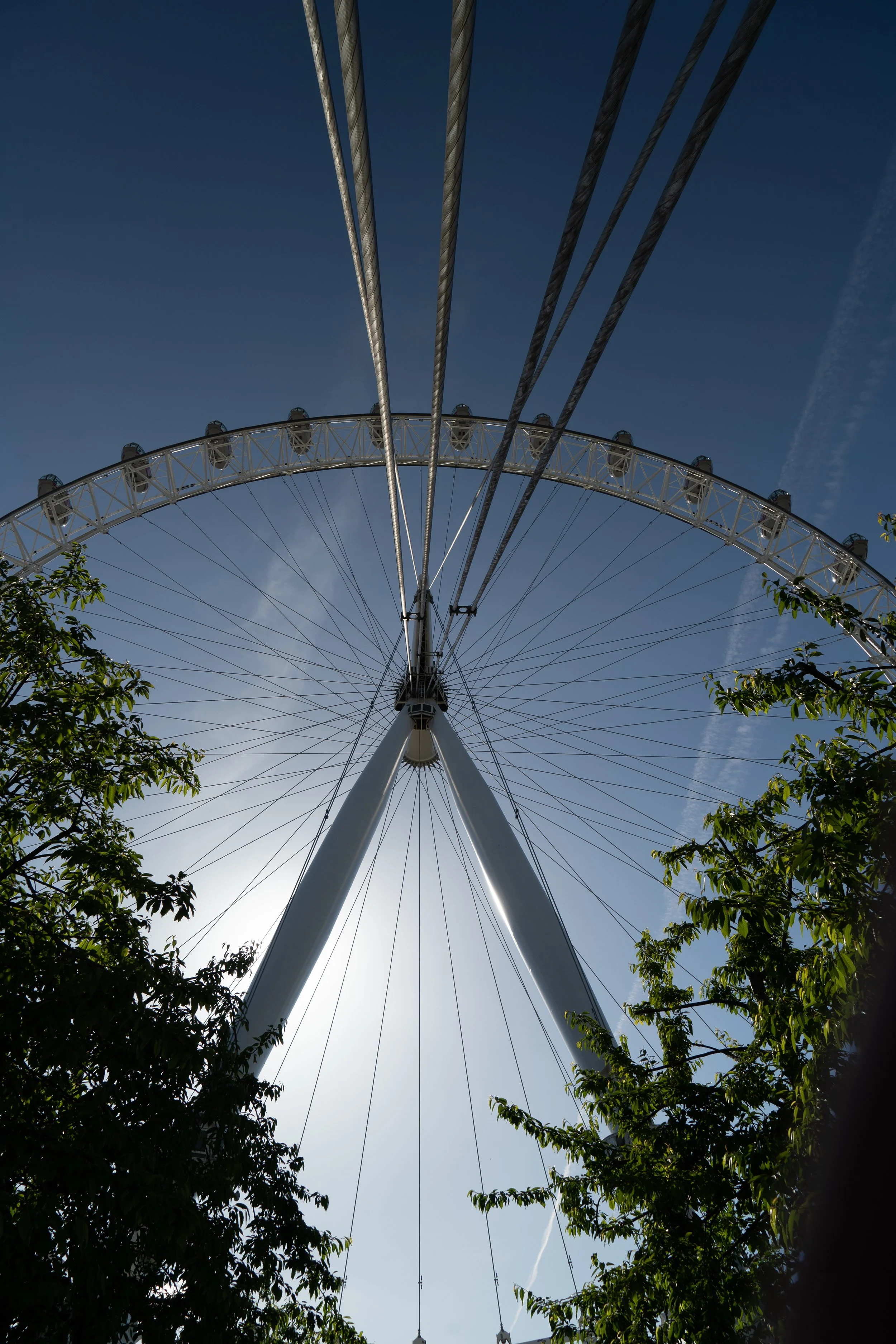 Looking up at a Ferris wheel with clear blue sky in the background and trees in the foreground.