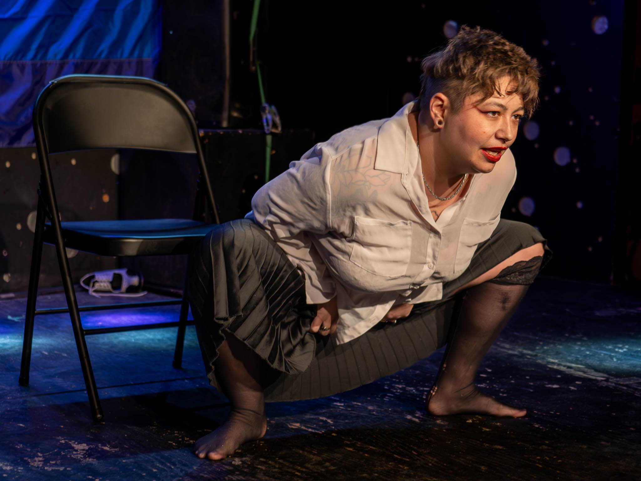Performing artist in expressive pose on stage next to a chair