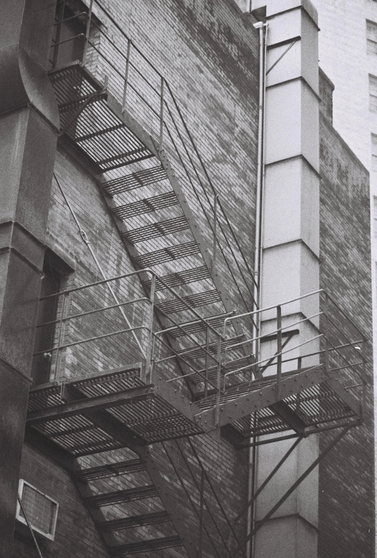 Black and white photo of a metal fire escape attached to a brick building.