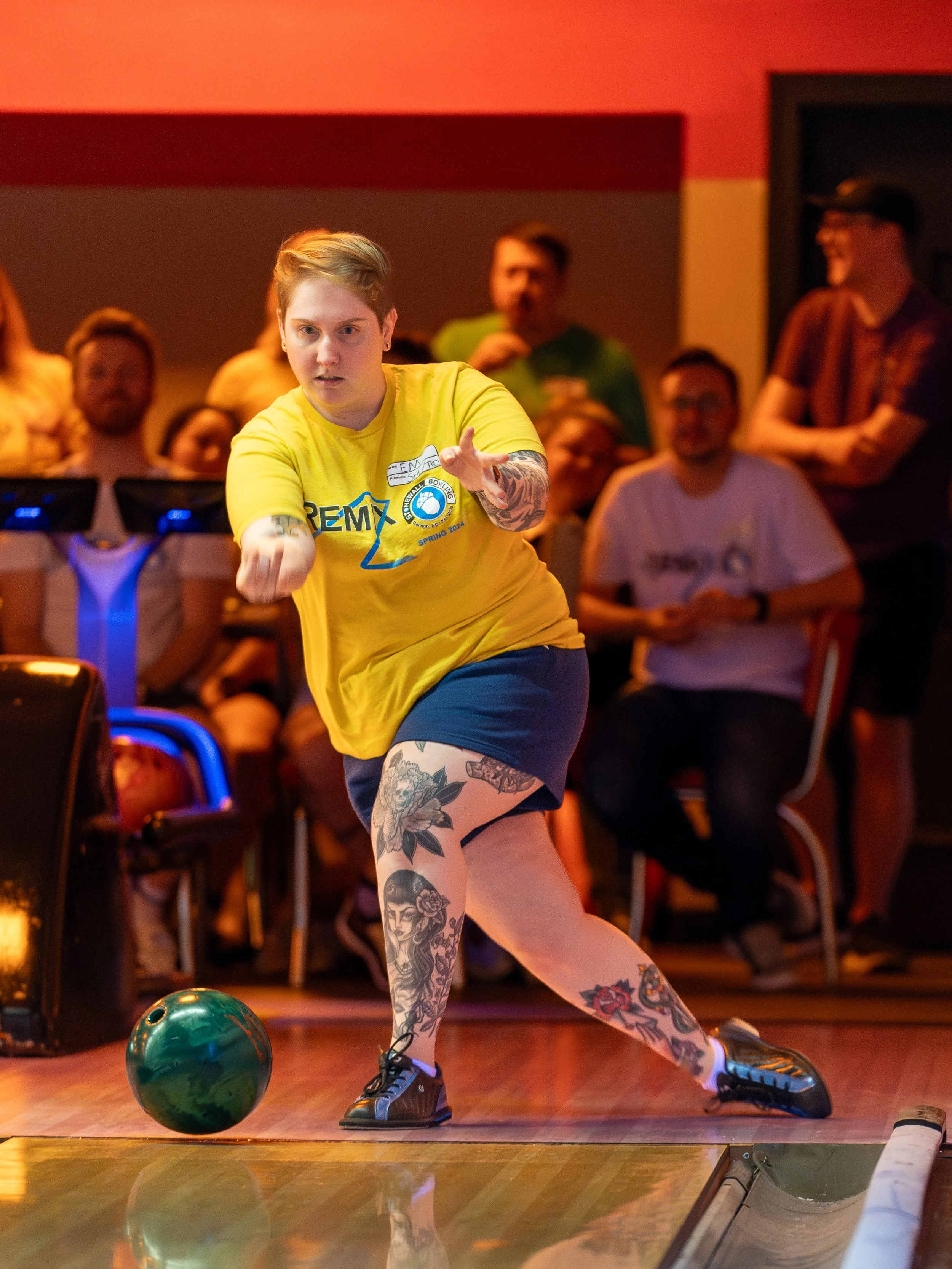 Person bowling on a lane wearing a yellow shirt and black shoes with a green bowling ball.