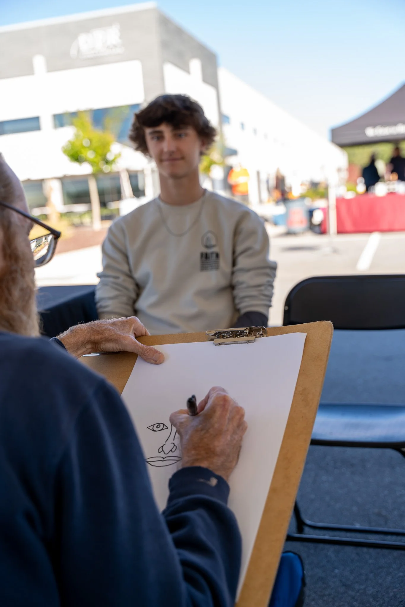 Artist sketching a seated young man on a clipboard outdoors