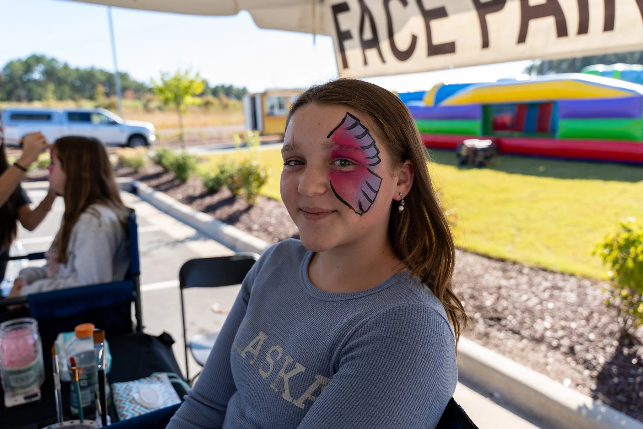 Girl with pink butterfly face paint at an outdoor festival with an inflatable bounce house