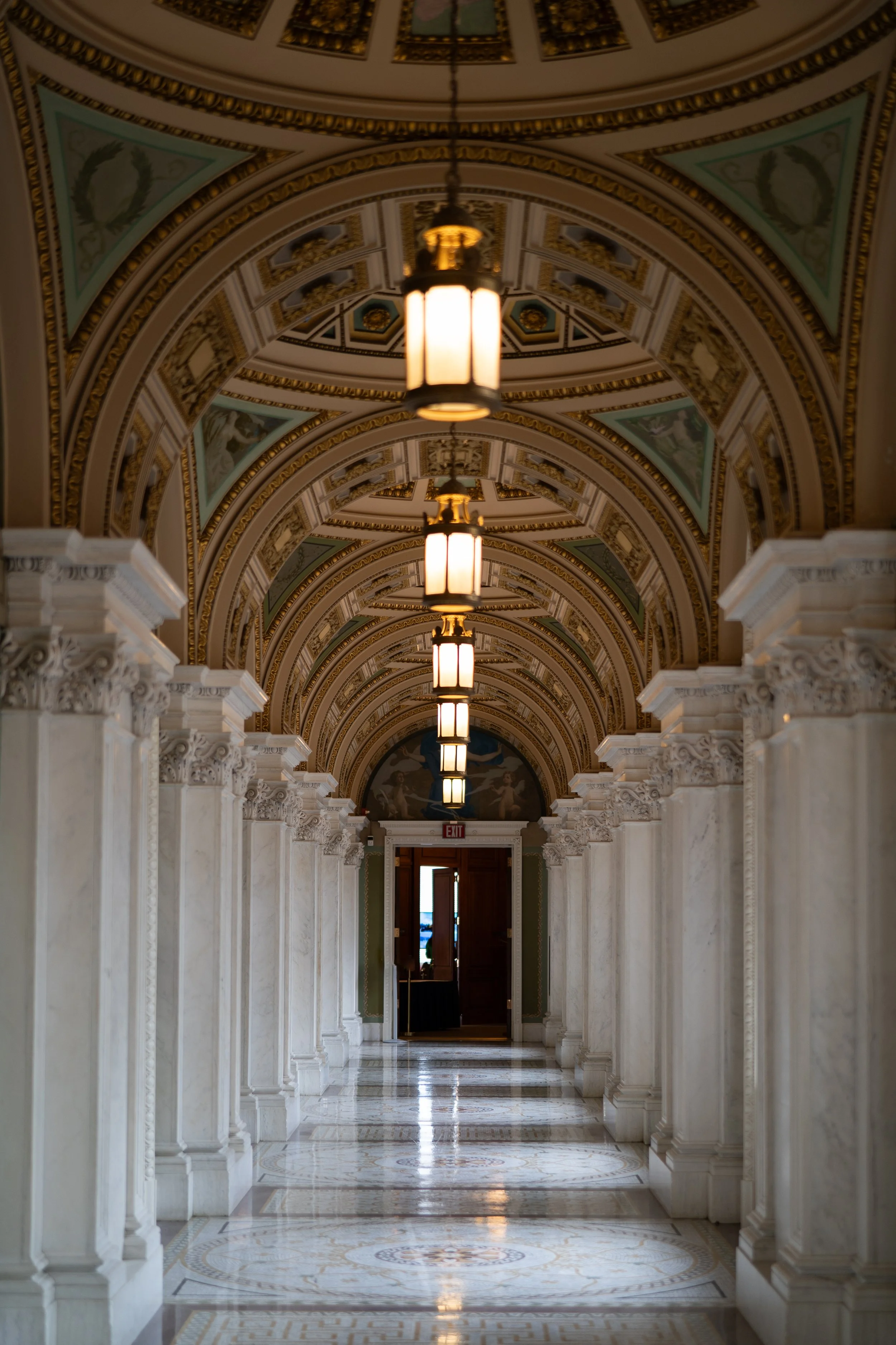 Ornate corridor with arched ceiling, marble columns, and hanging lanterns.
