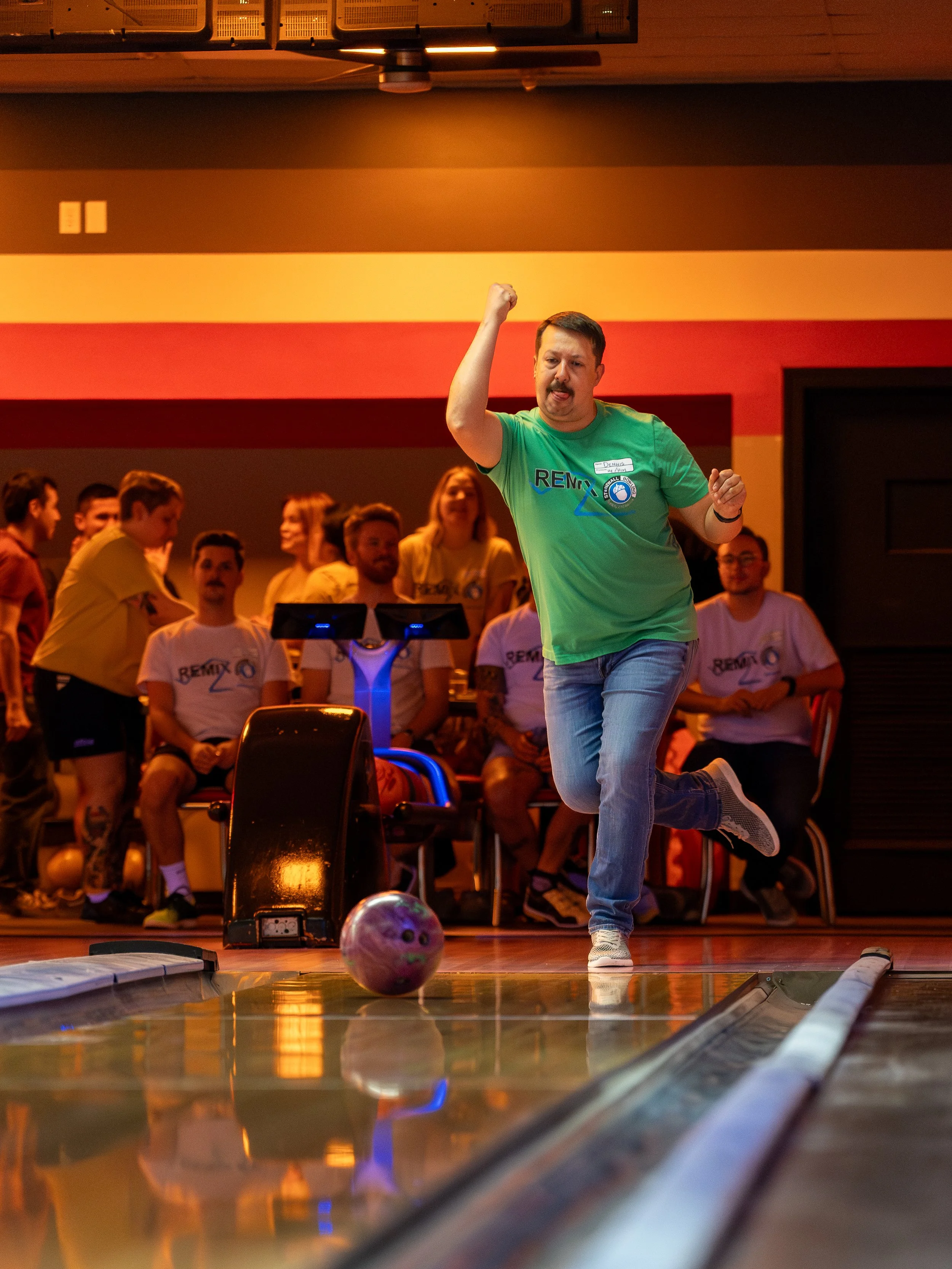 Man celebrating a successful bowling shot in a bowling alley, surrounded by spectators.
