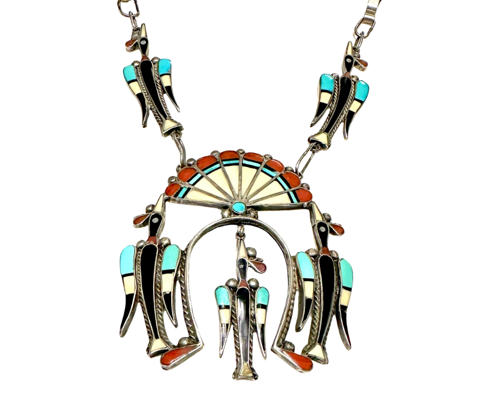 A silver necklace with turquoise, red, and cream stone inlay design, featuring a large circular pendant with a radiating pattern and hanging feather-shaped charms.