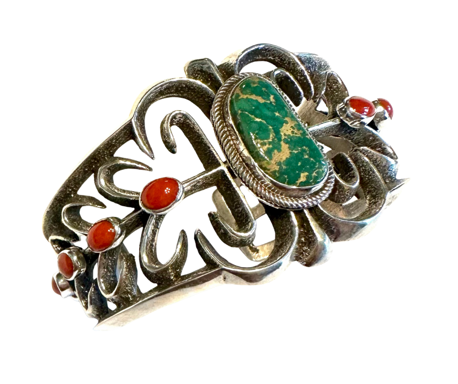Silver ring with intricate floral design, featuring red and green gemstones.
